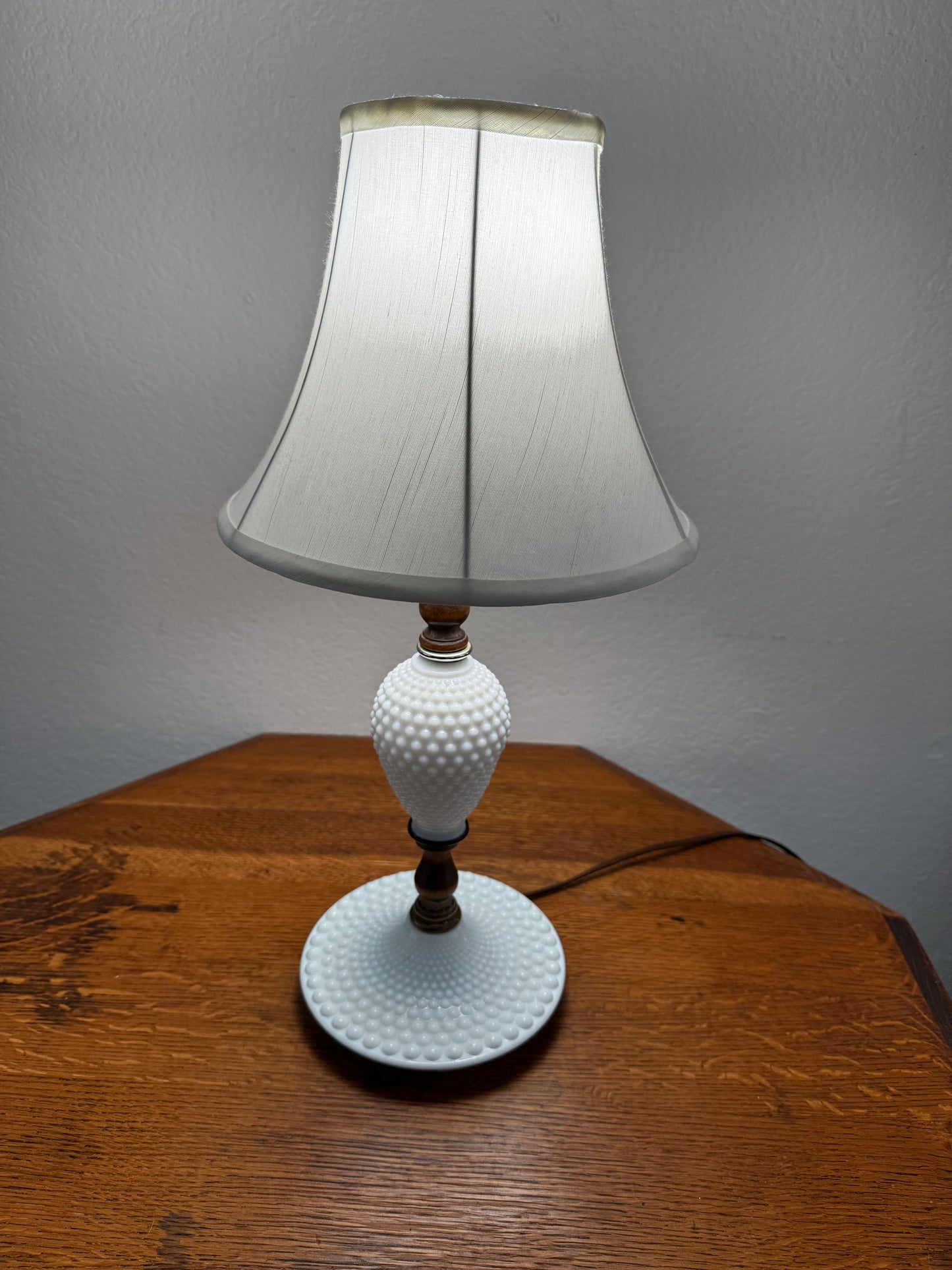 Hobnail milk Lamp with white textured shade on a wooden surface against a gray wall