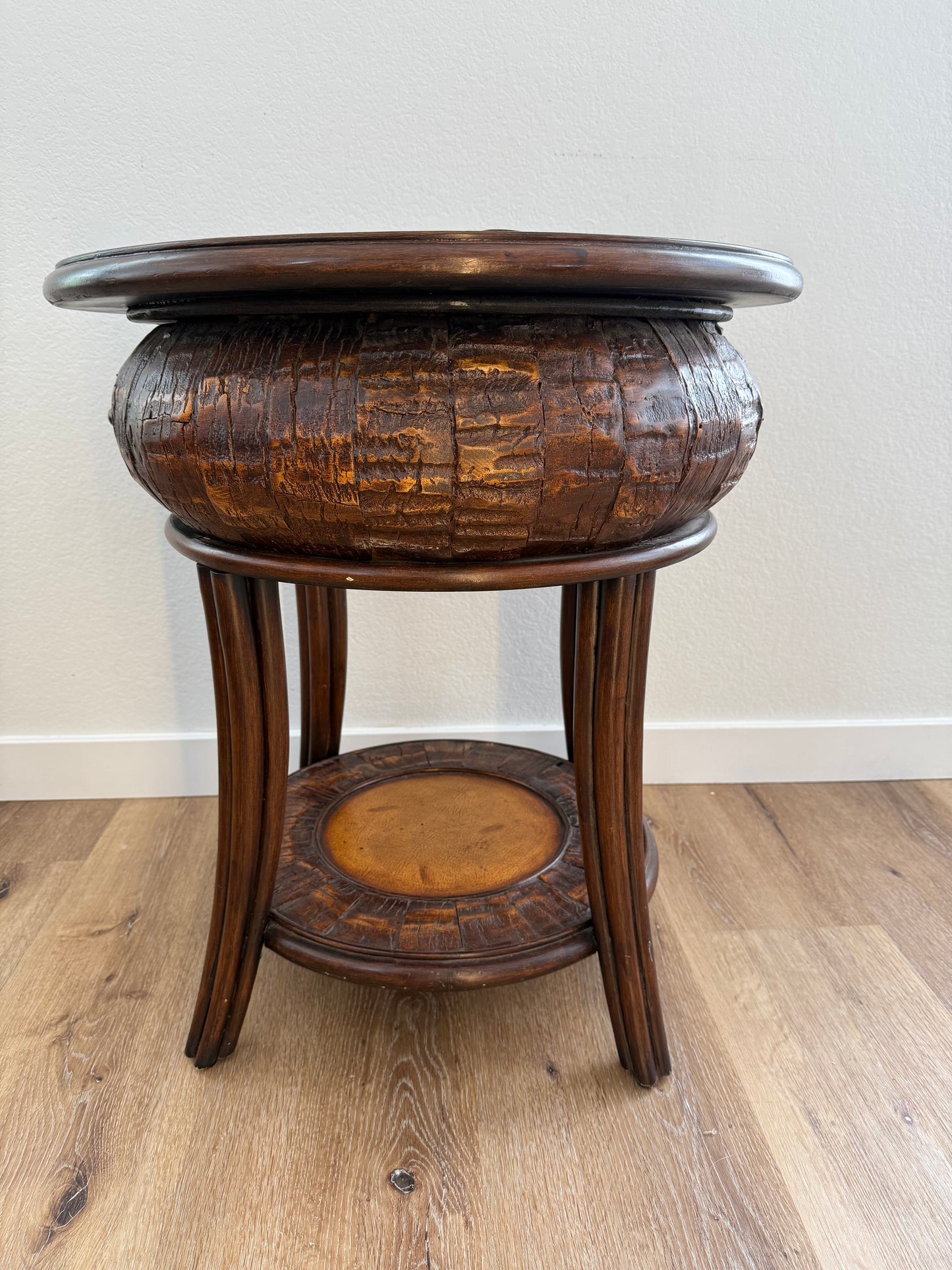 Round side table with a textured surface and a shelf on a wooden floor.
