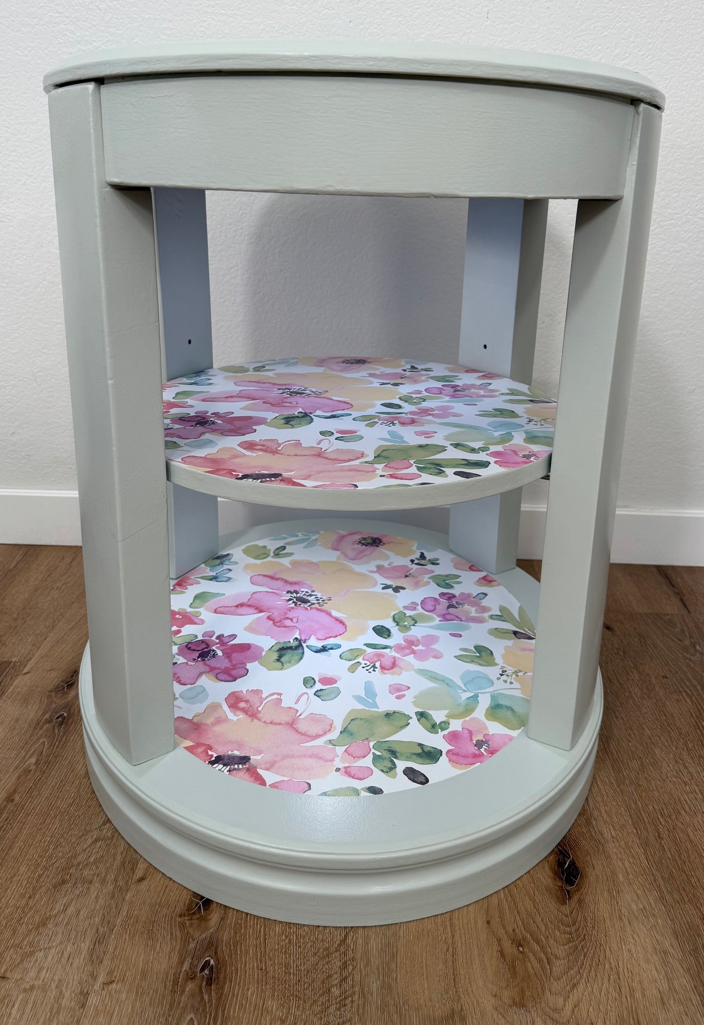 Oval side table with floral-patterned shelves on a wooden floor.