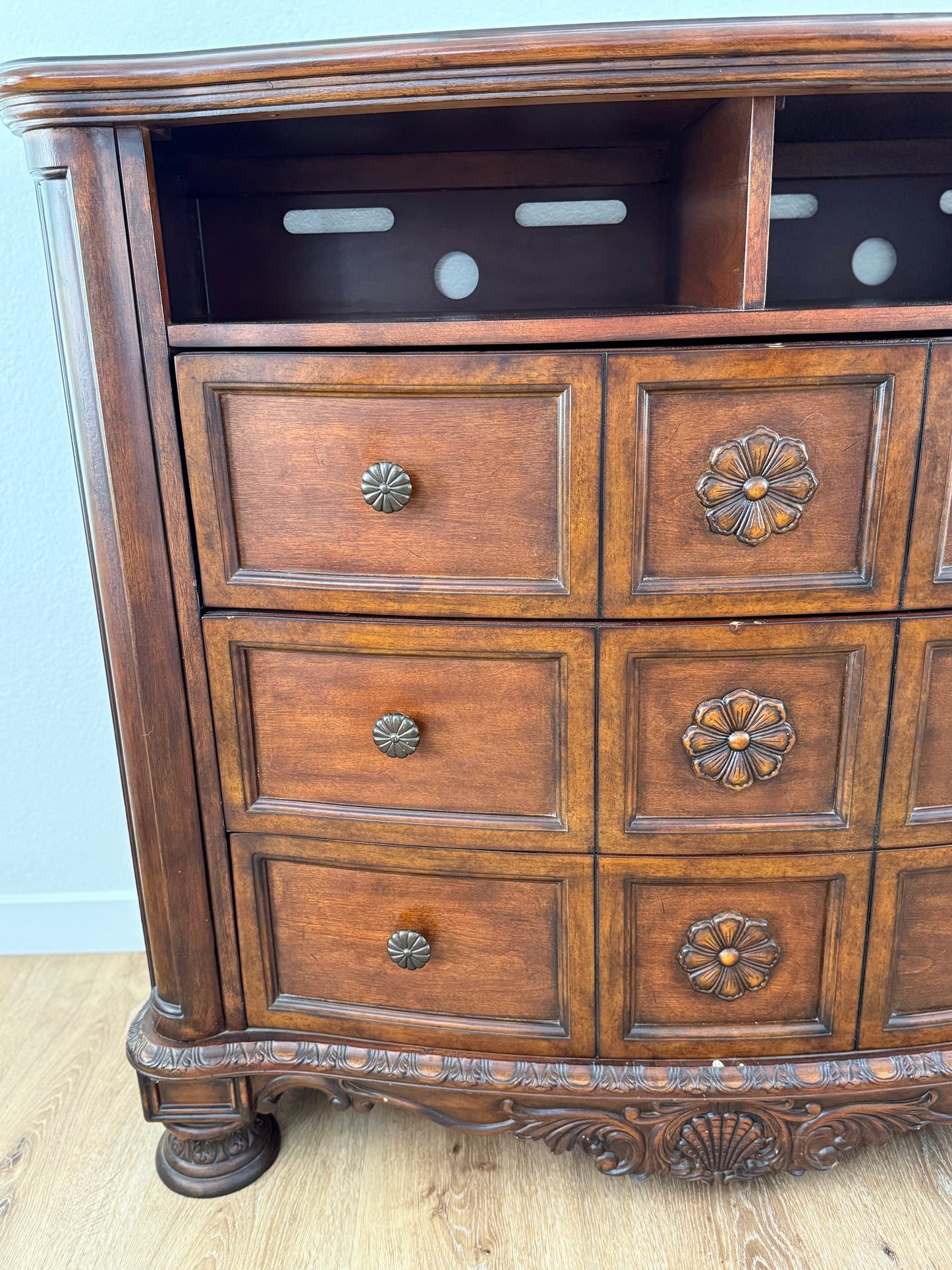 Wooden dresser with decorative drawers and carvings on a light blue wall background