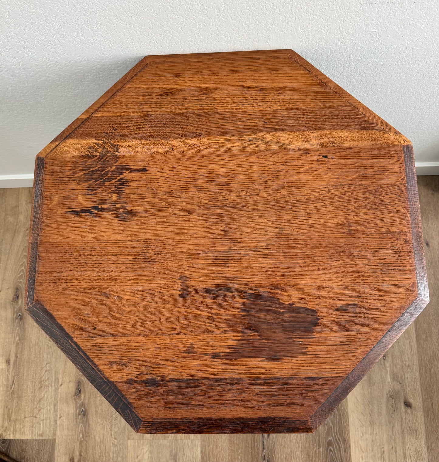 Octagonal wooden table top on a wooden floor with a white wall background