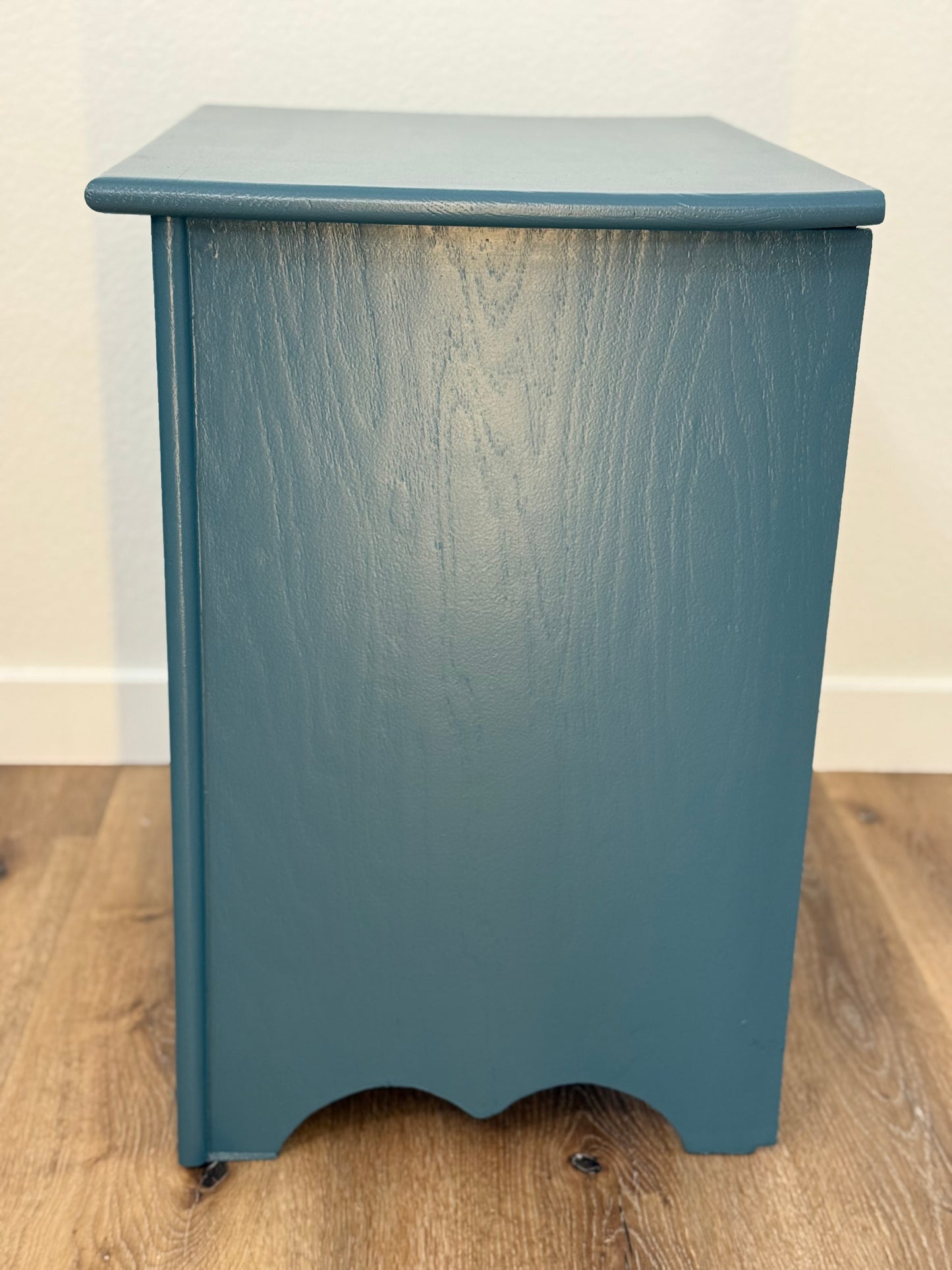 Blue wooden side table on a wooden floor with a white wall background