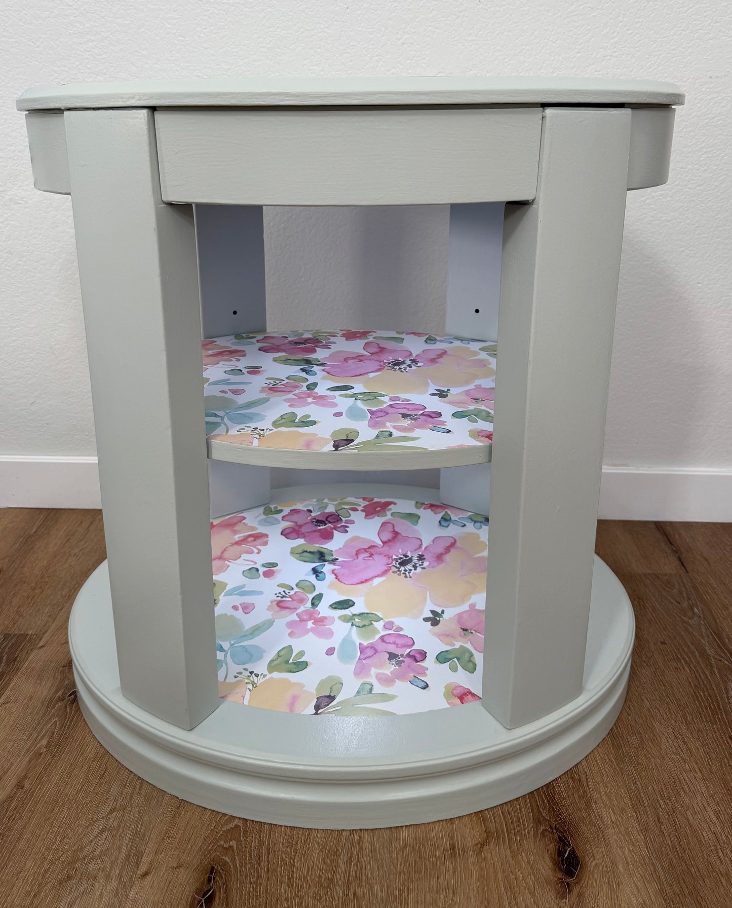 Oval side table with floral-patterned shelves on a wooden floor.