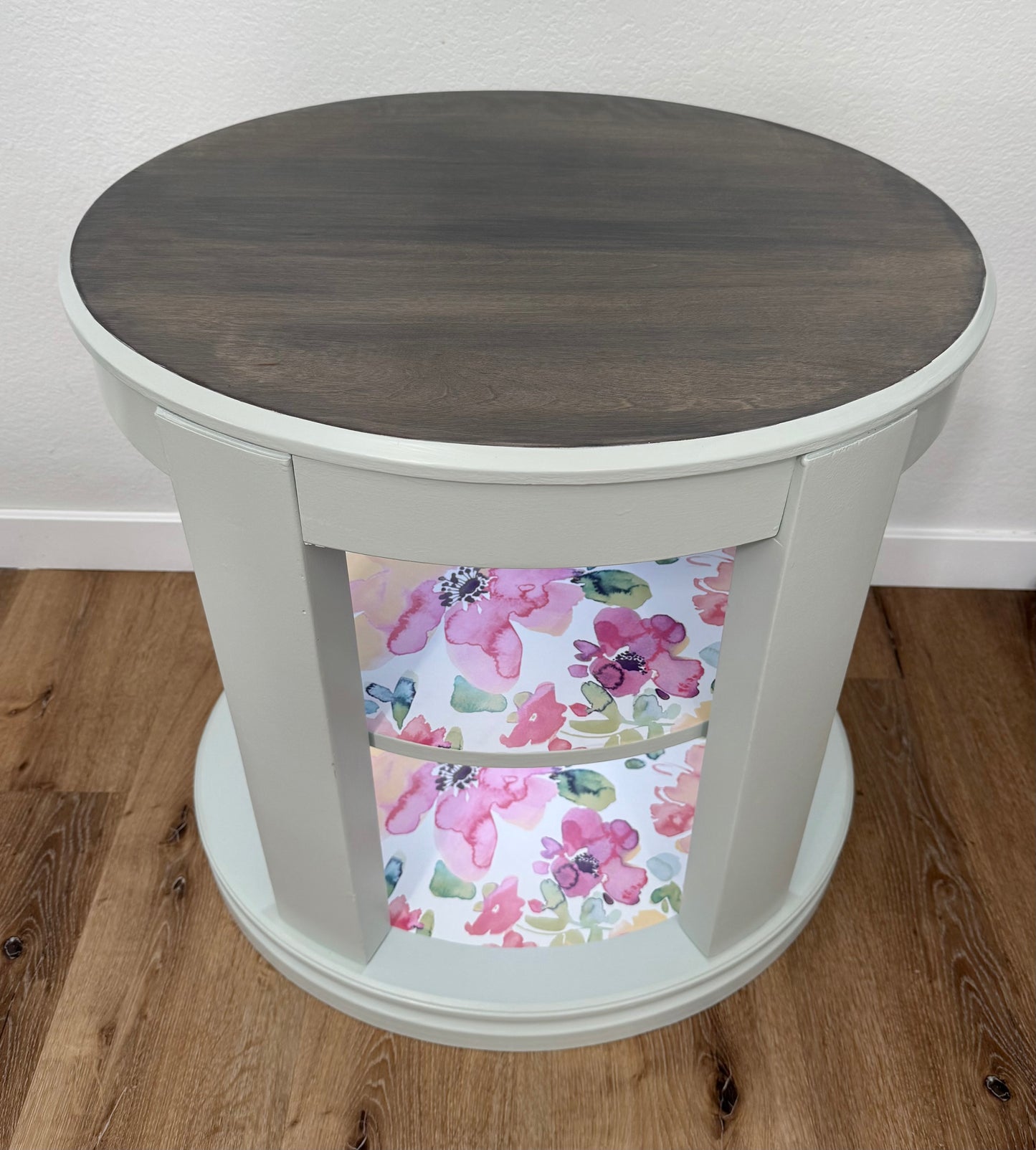 Oval wooden side table with floral patterned shelves on a wooden floor.