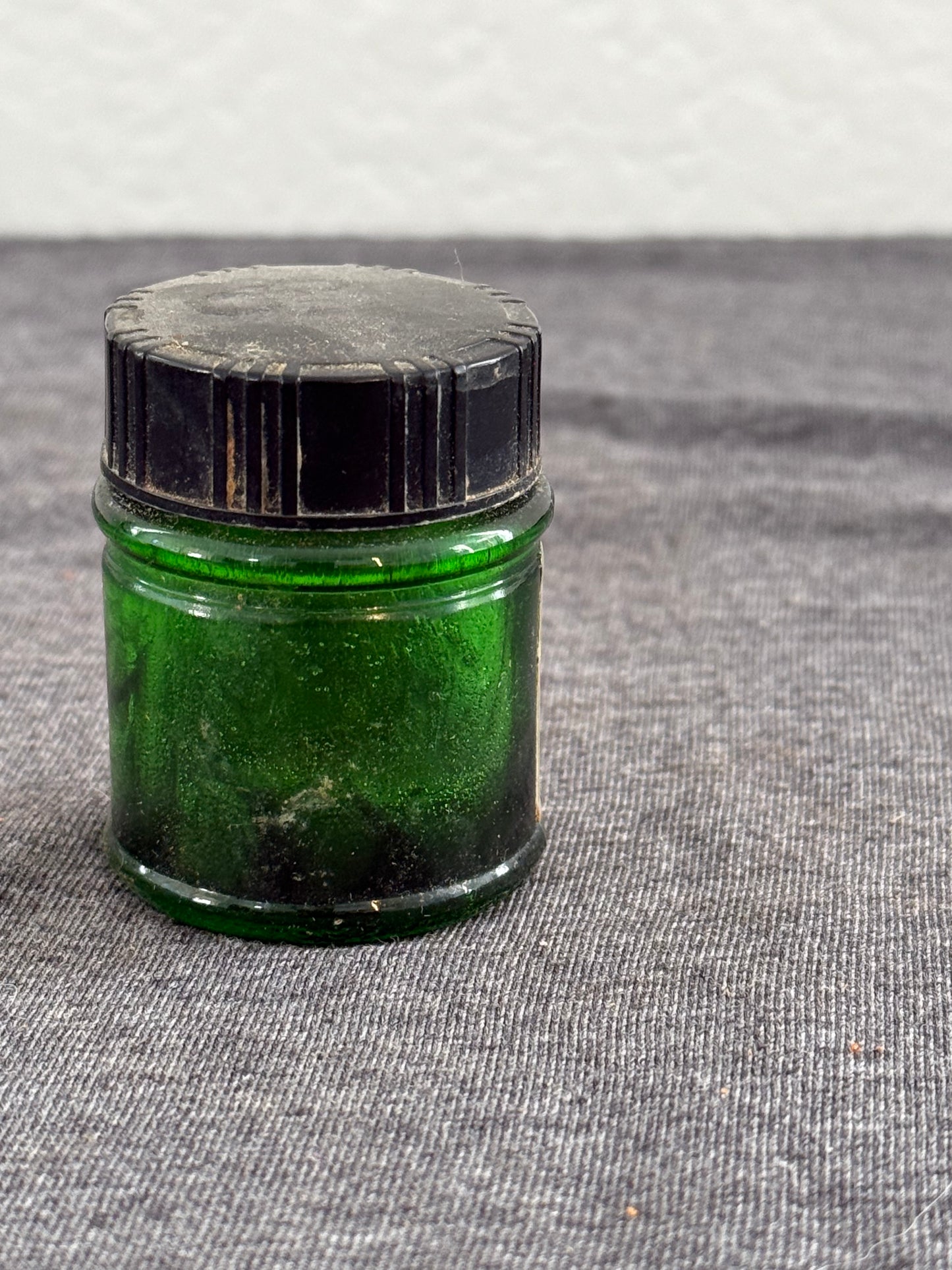 Small green glass bottle with a silver cap on a textured gray background