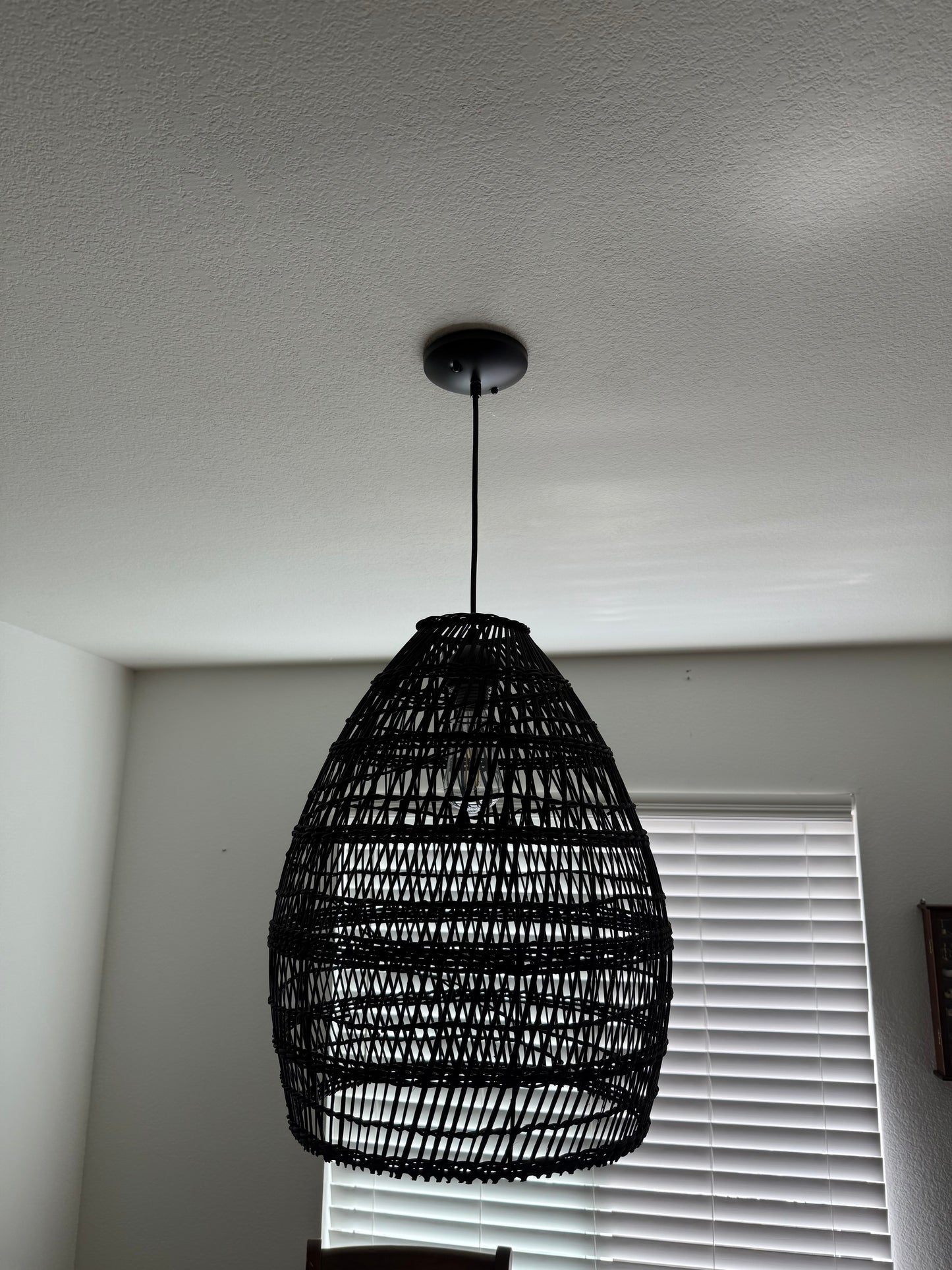 Black woven wall light fixture on a plain wall.