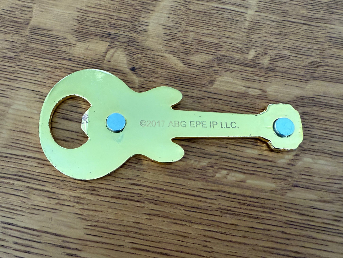 Metallic guitar-shaped bottle opener on a wooden surface
