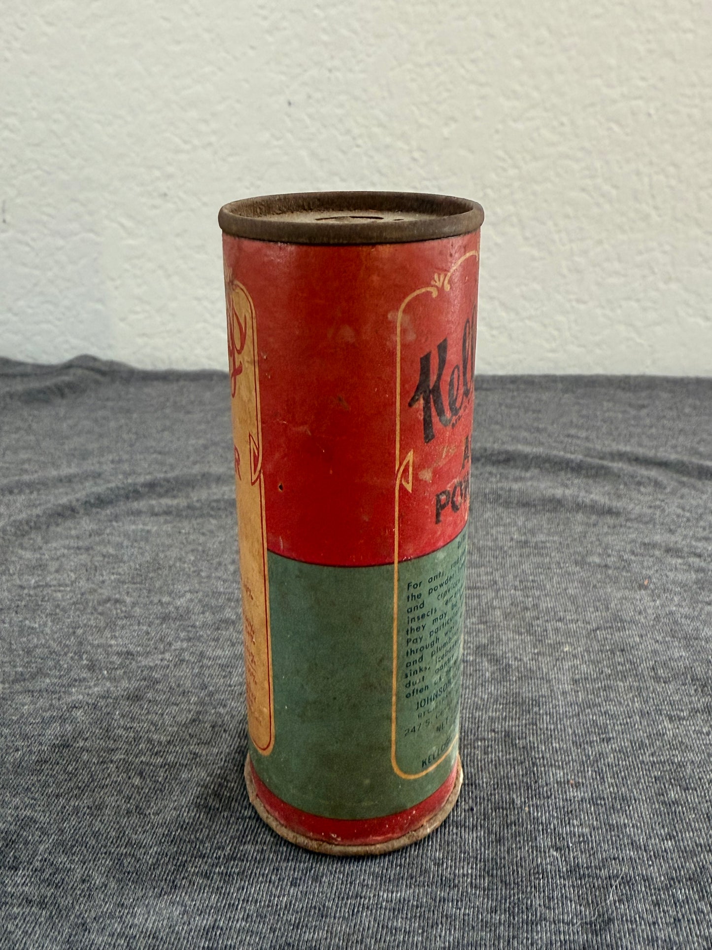 Vintage cylindrical container with red and green design on a textured surface