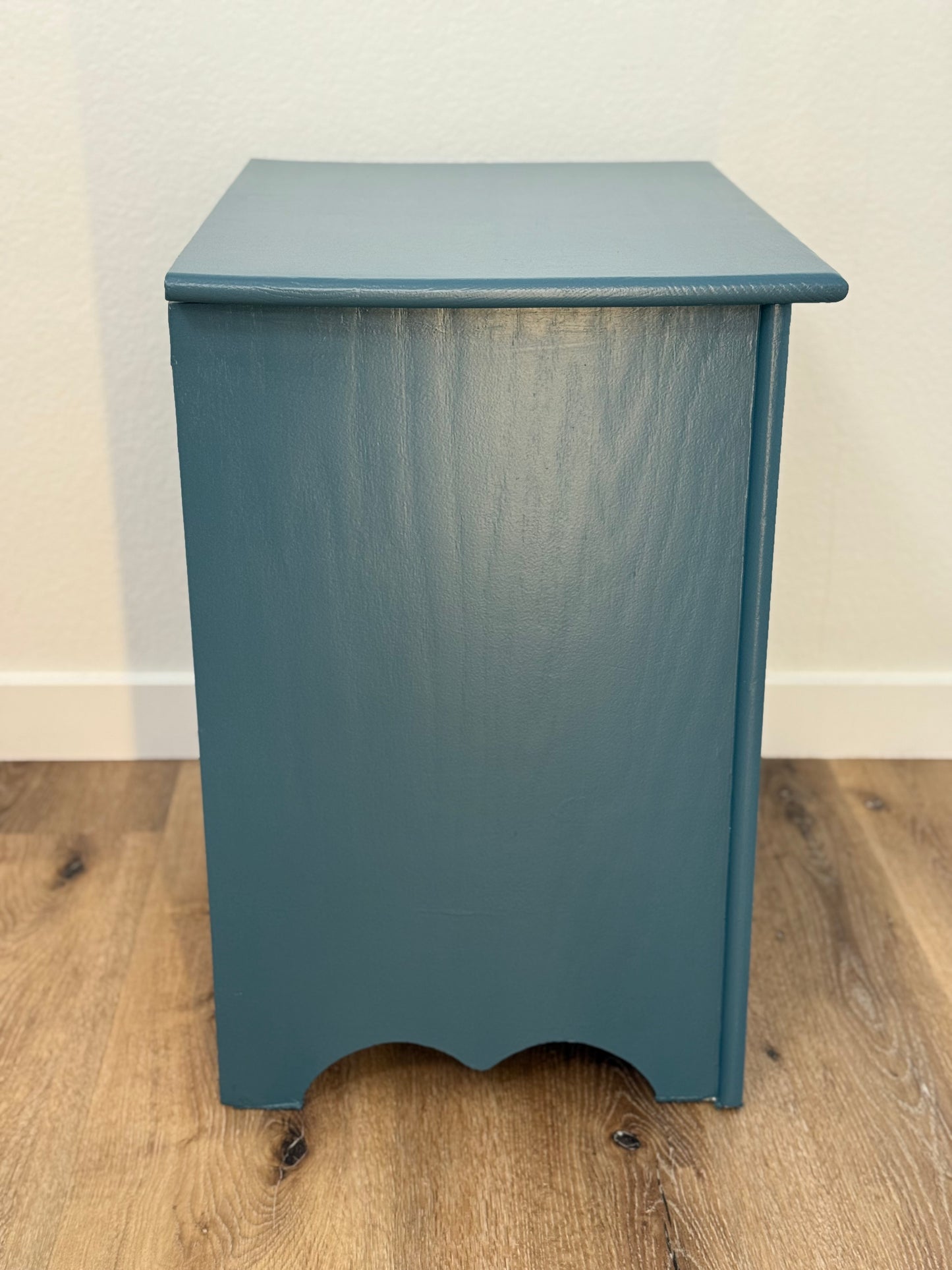 Blue wooden side table on a wooden floor with a white wall background