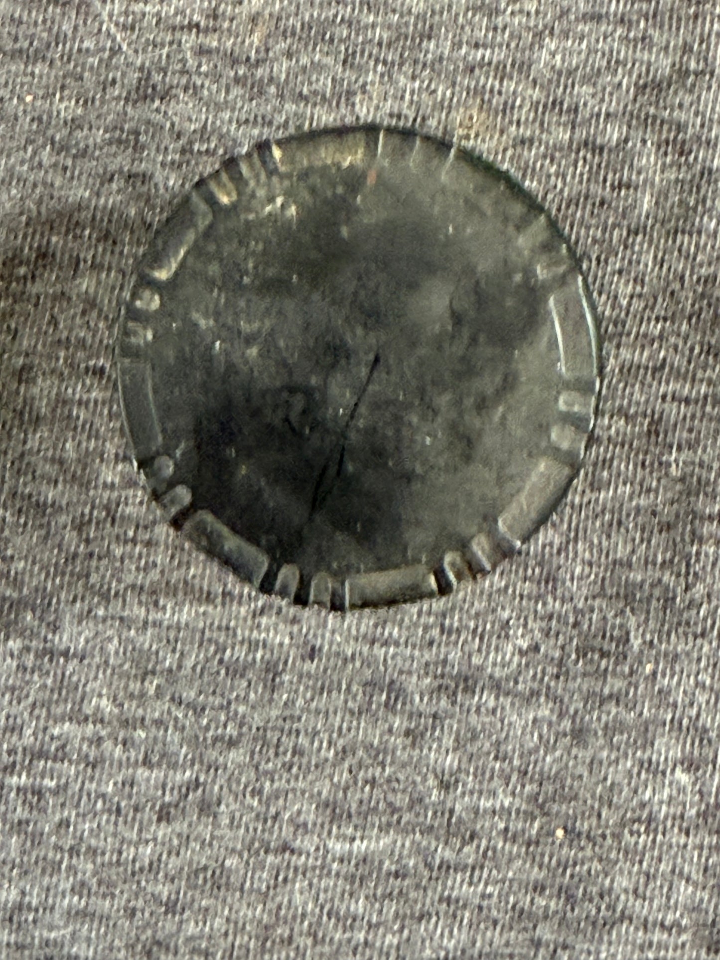 Circular metallic object with textured edge on a gray fabric background