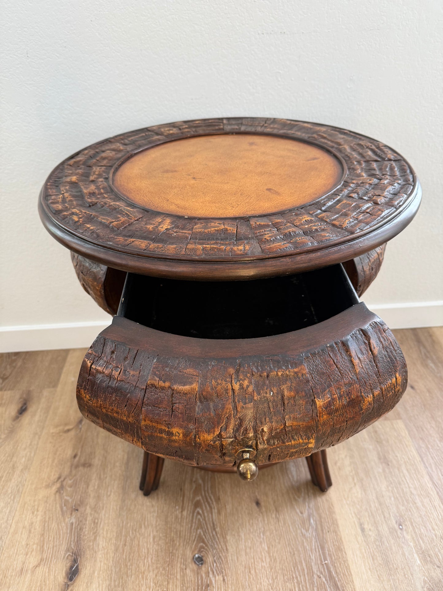 Round side table with a textured surface and an open drawer on a wooden floor.