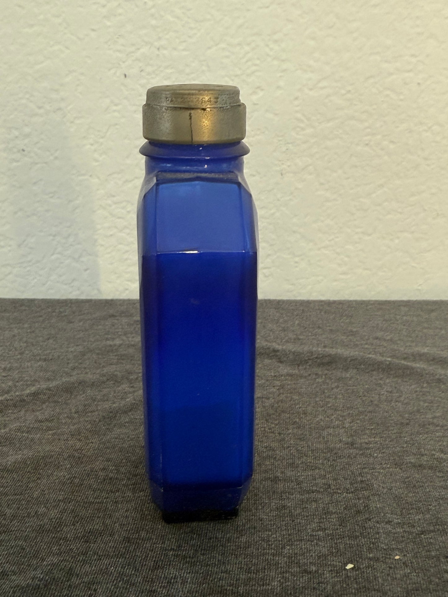 Cobalt blue talcum bottle with a metallic cap on a white and gray surface