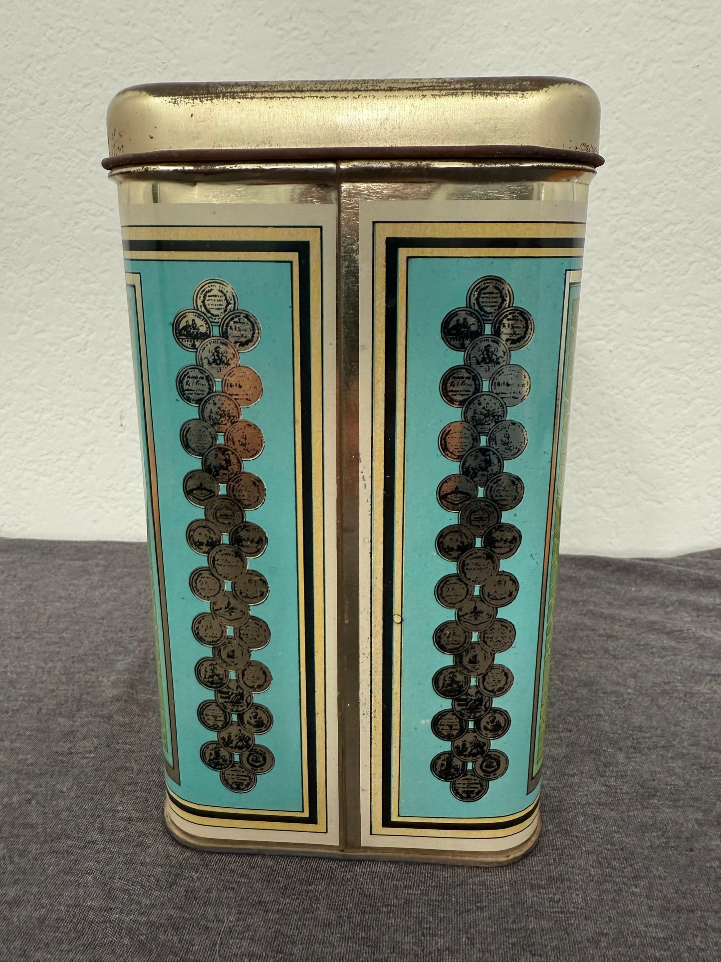 Decorative tin box with turquoise and gold design on a gray surface
