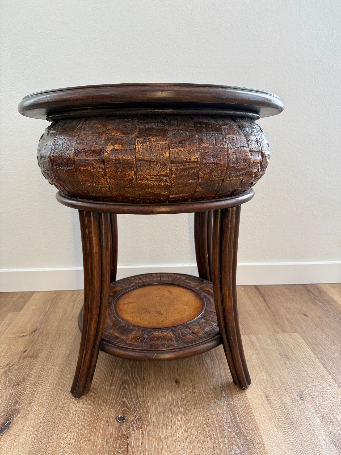 Round side table with a textured surface and a shelf on a wooden floor.