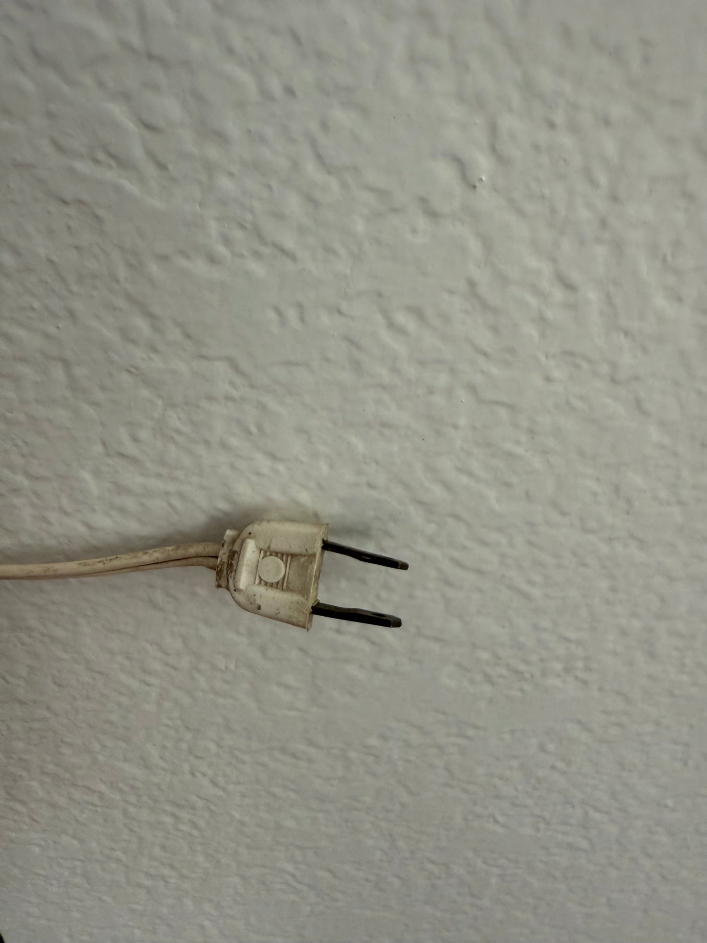 Old electrical plug on a textured white wall