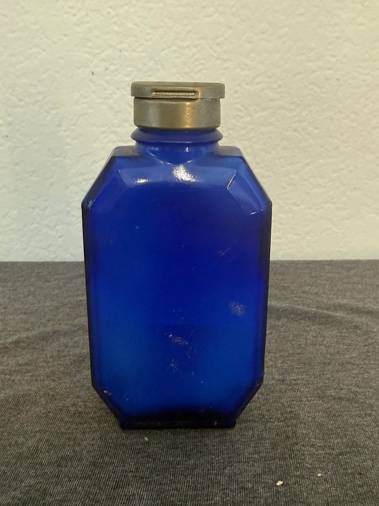 Blue glass bottle with a silver cap on a gray and white surface