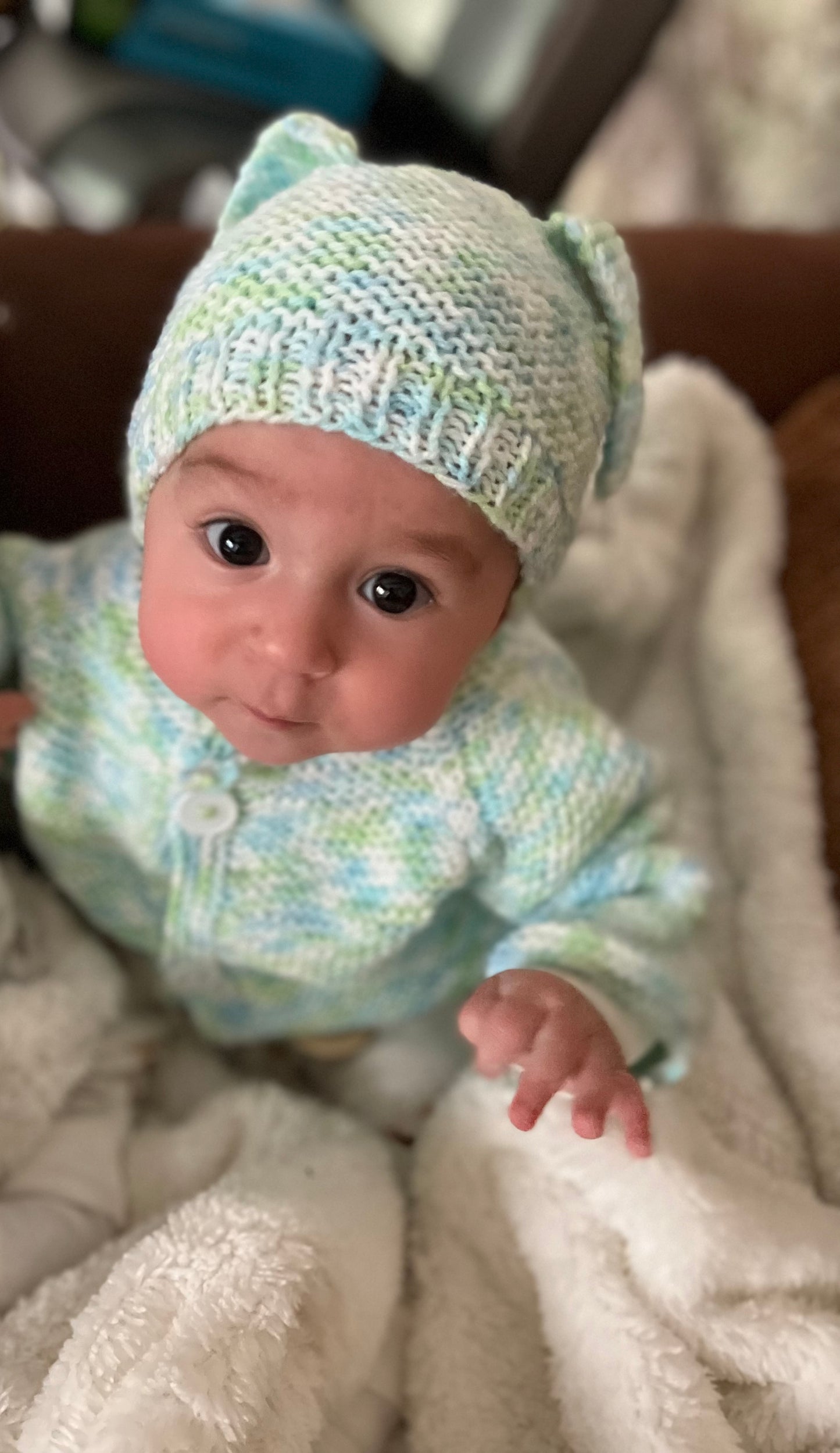 Baby wearing a knitted outfit and hat on a soft surface