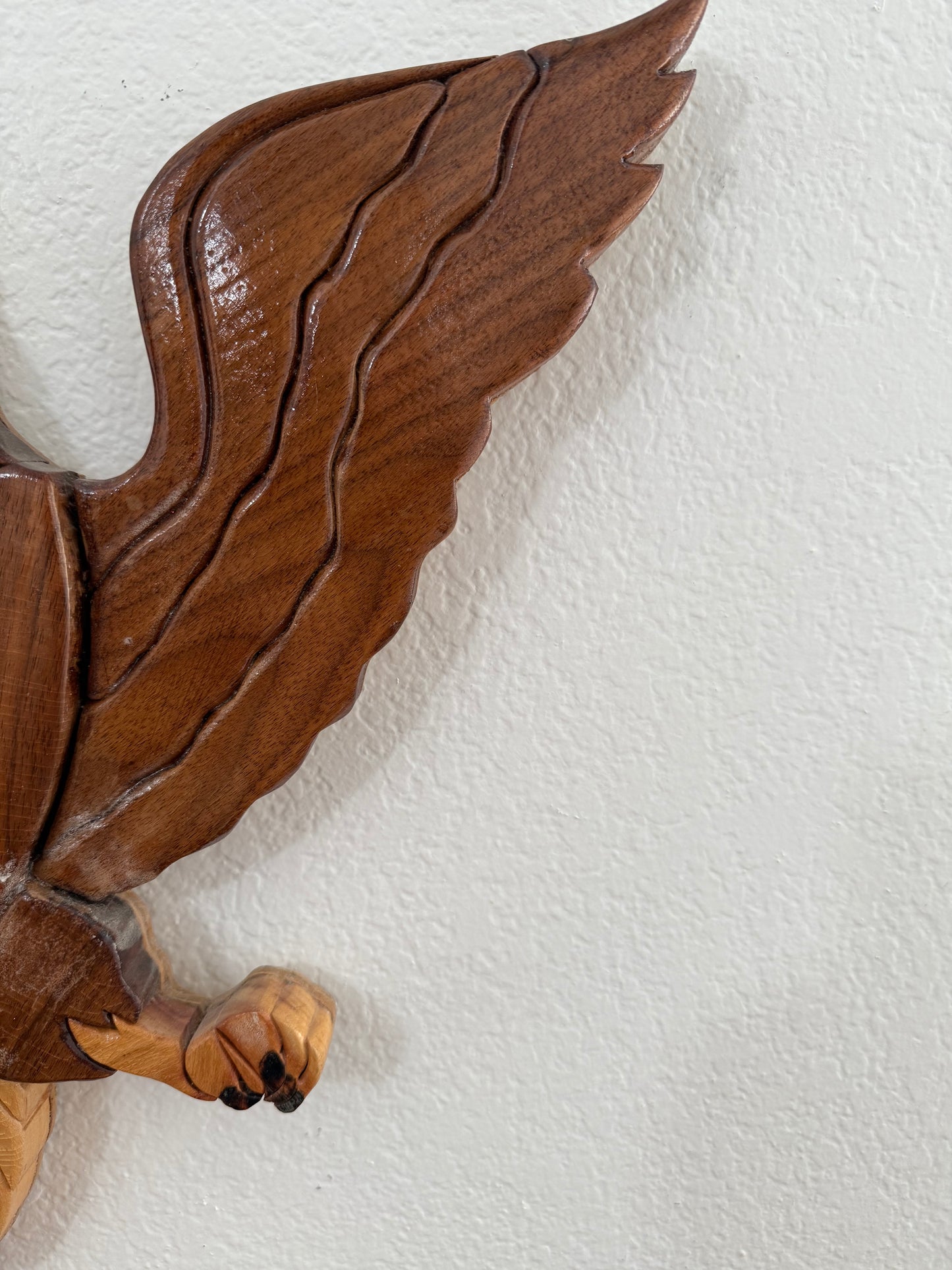 Wooden sculpture of a winged creature on a textured white background