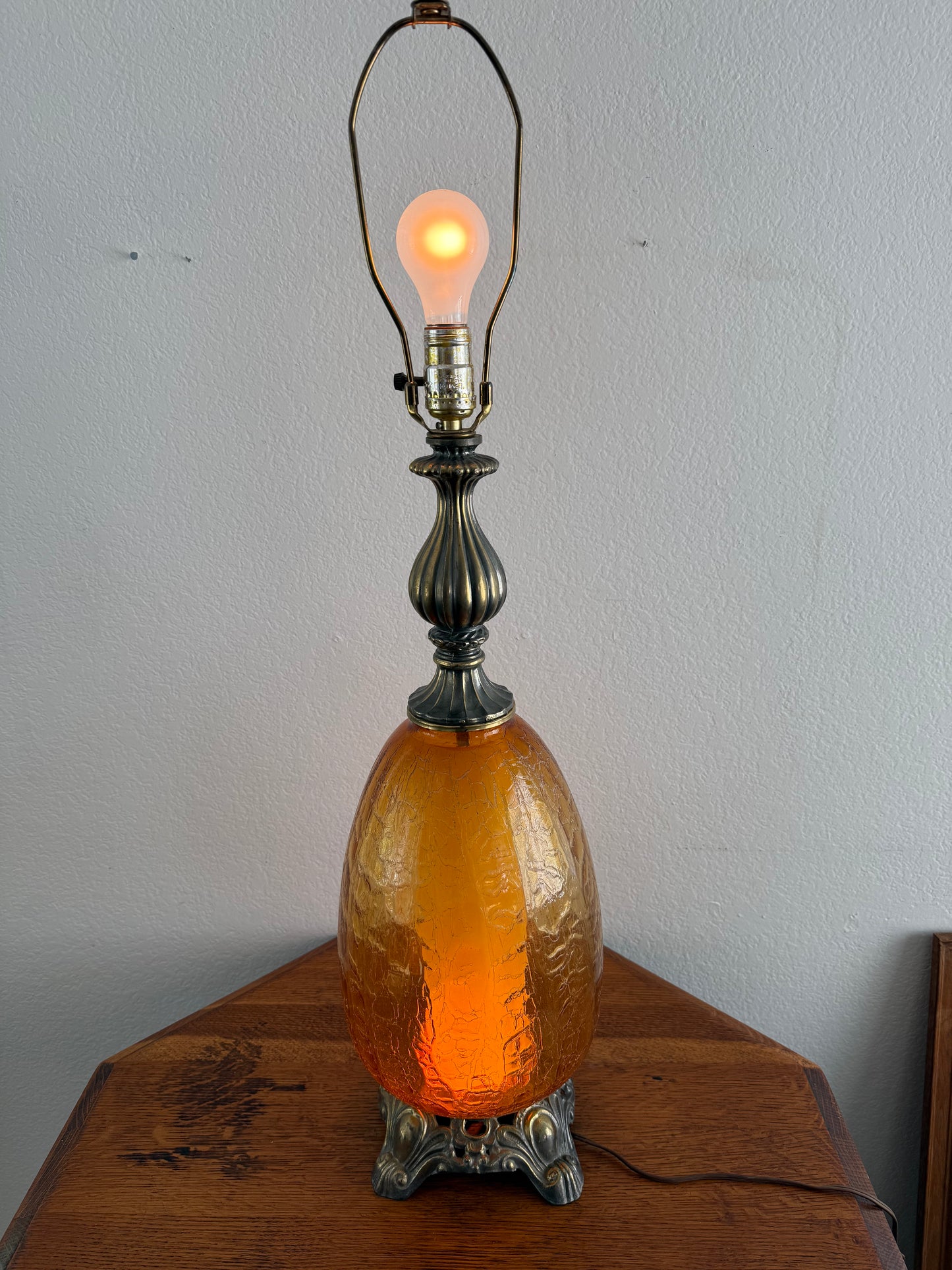 Decorative lamp with amber glass shade and visible light bulb on a wooden base against a white wall.