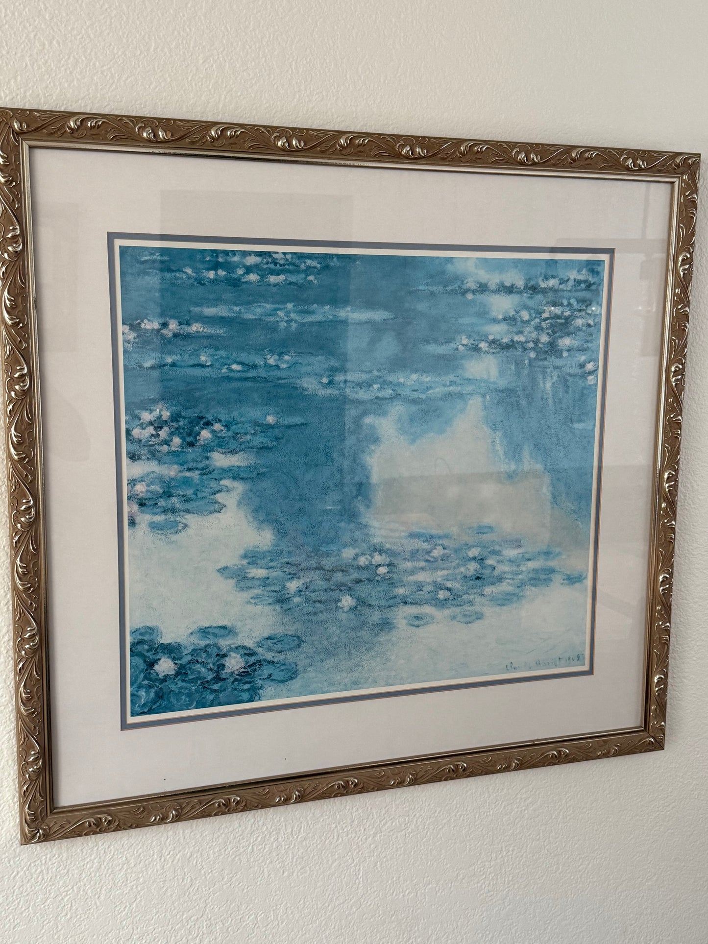 Framed abstract artwork with blue and white tones on a plain wall.