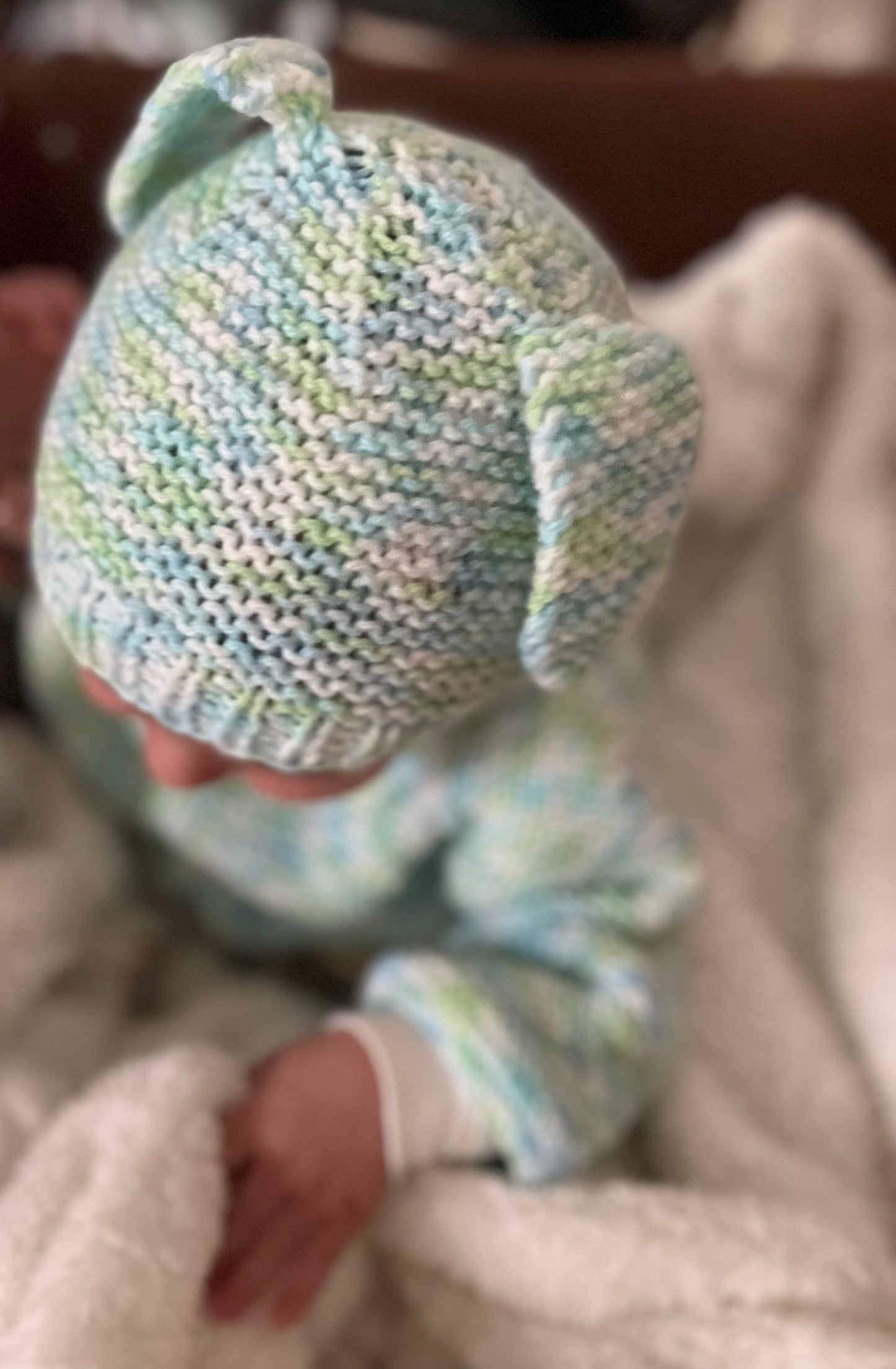 Baby wearing a knitted hat and outfit on a soft surface