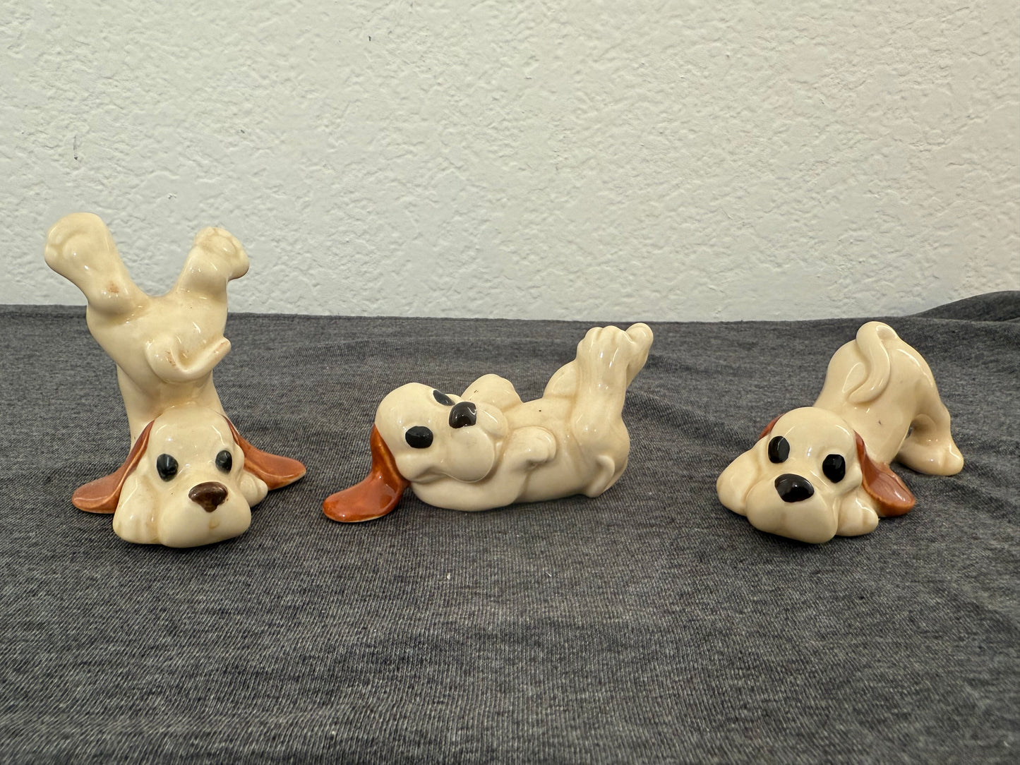 Three ceramic dog figurines on a gray surface with a white wall background