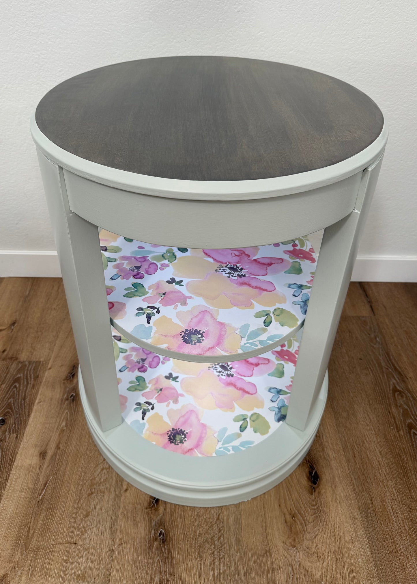 Round side table with a floral patterned shelves on a wooden floor.