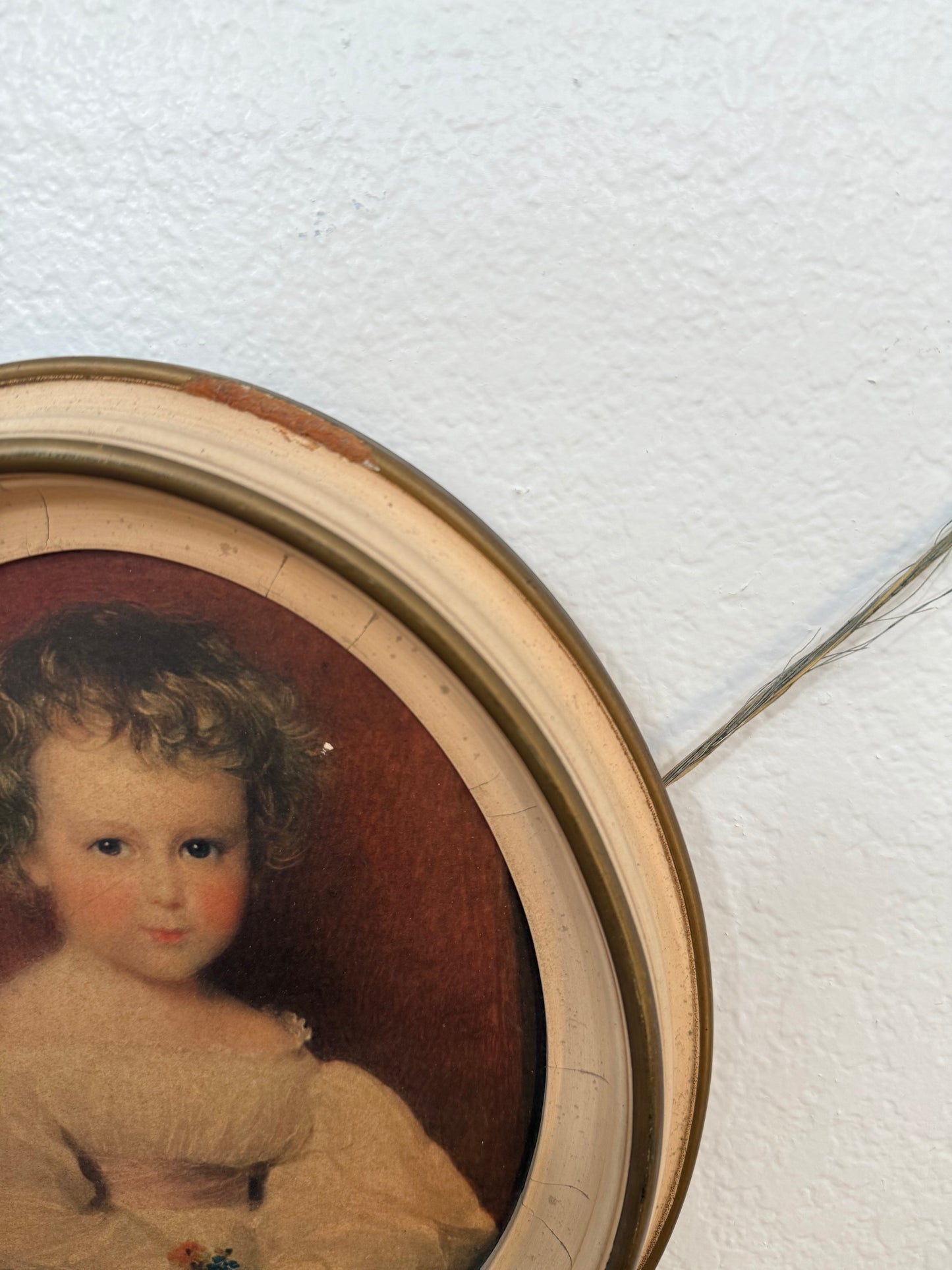 Vintage doll head painting in a round wooden frame against a white wall.