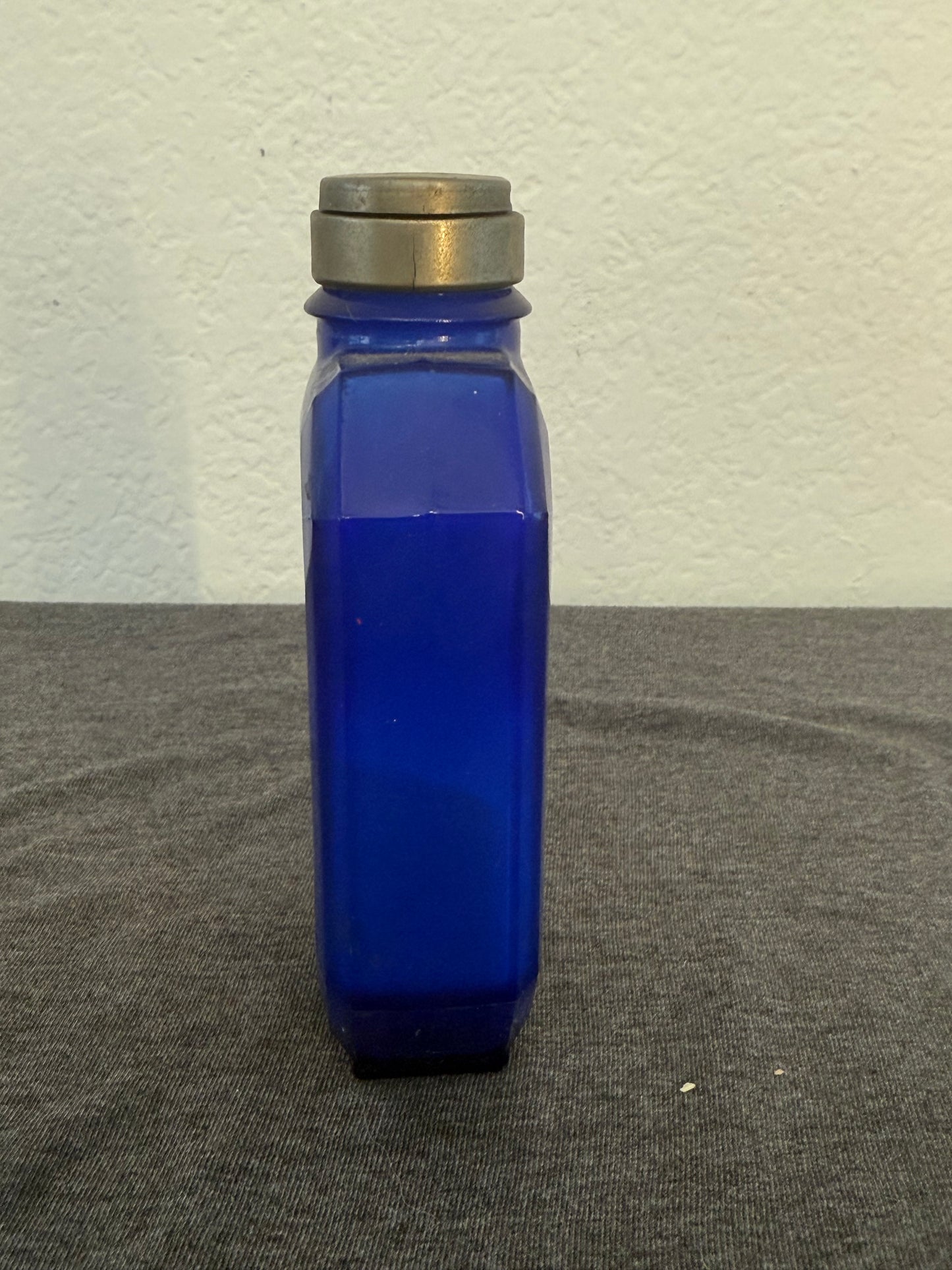 Blue glass bottle with silver cap on a gray surface