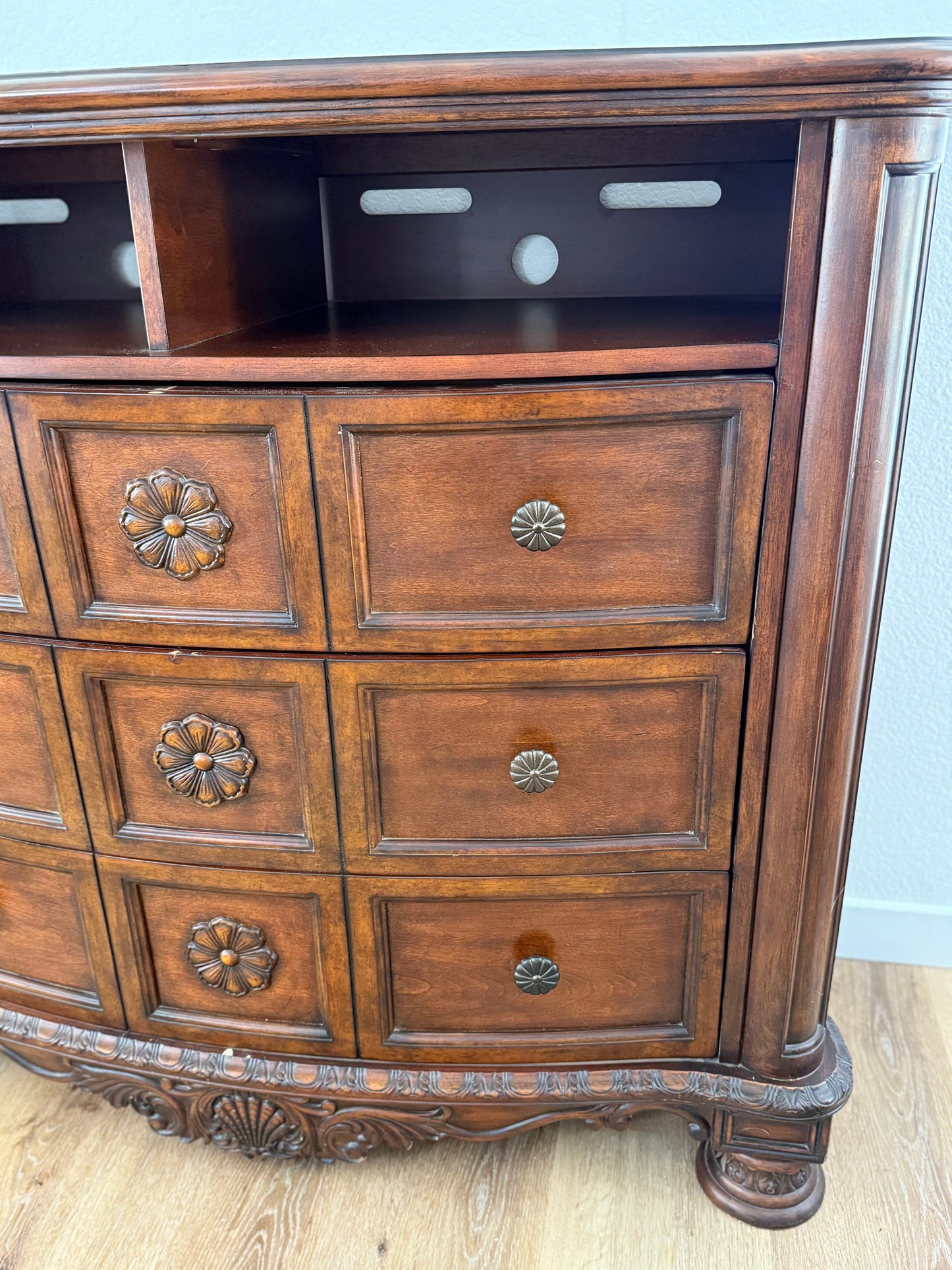 Wooden dresser with decorative drawers and carvings on a light wooden floor.