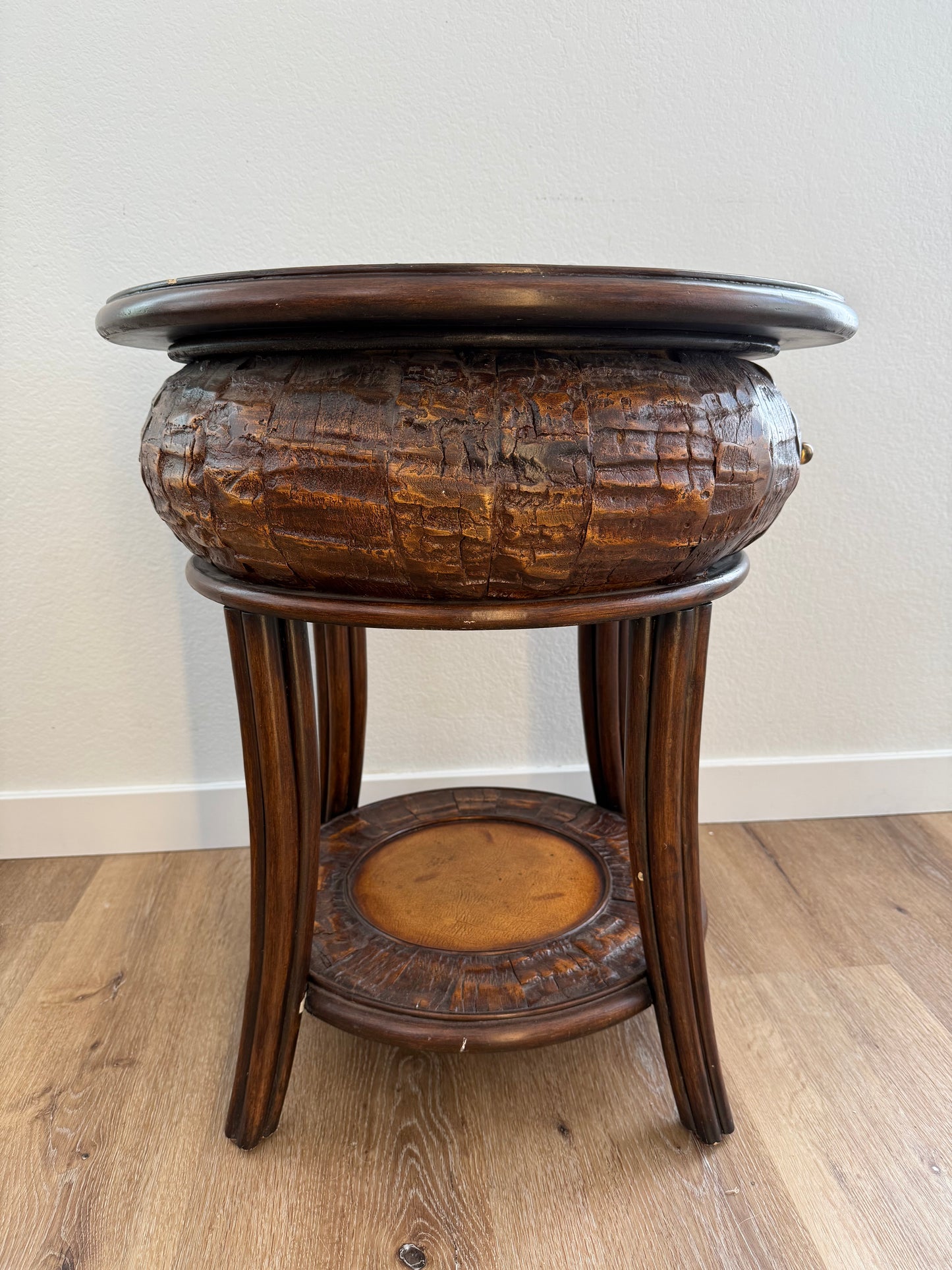Round side table with a textured surface and a shelf on a wooden floor.