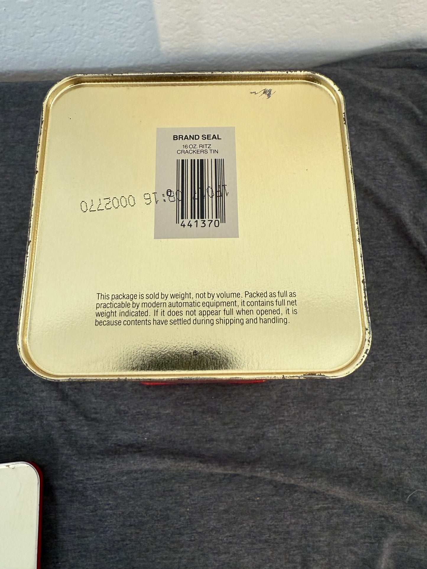 Gold compact mirror with brand seal and barcode on a gray surface