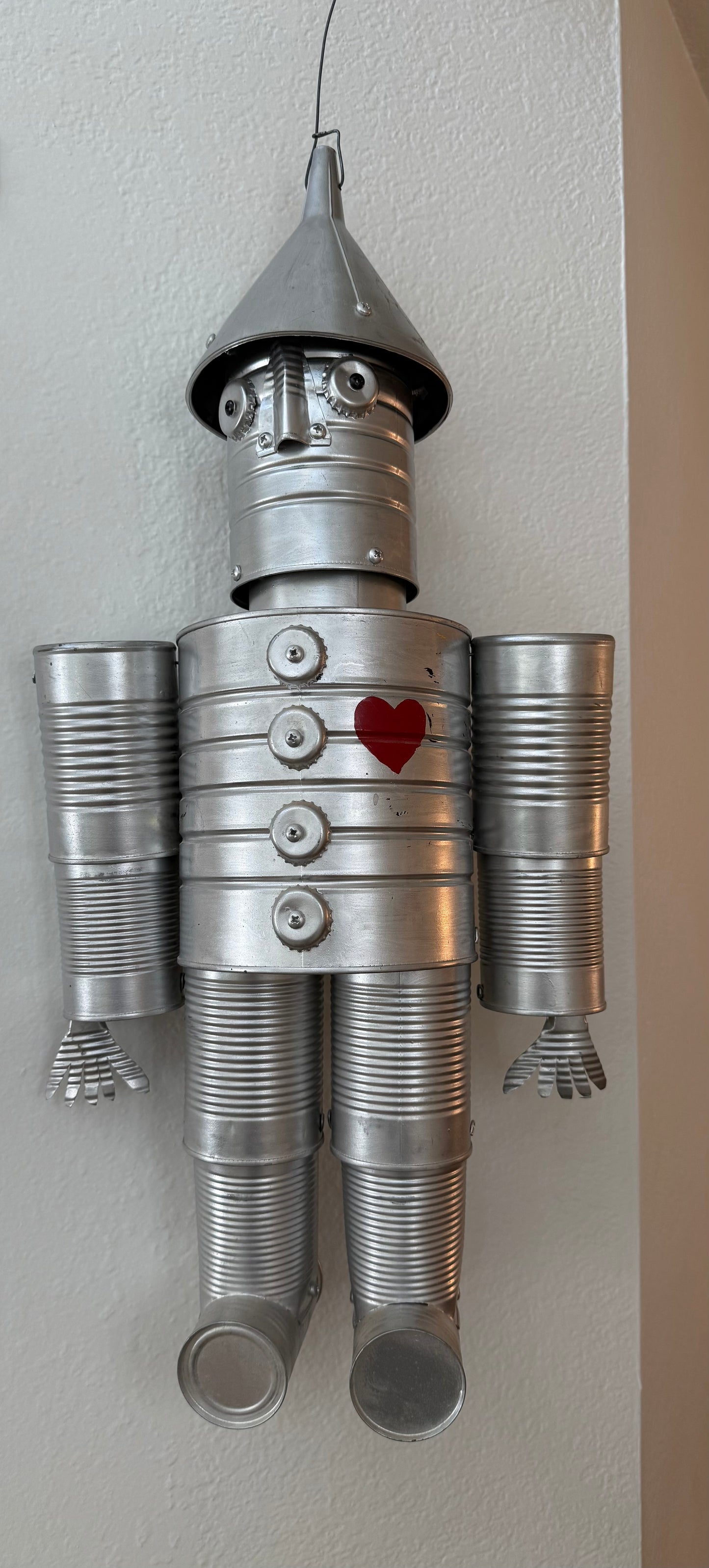 Metal tin man sculpture with a heart on its chest against a plain wall