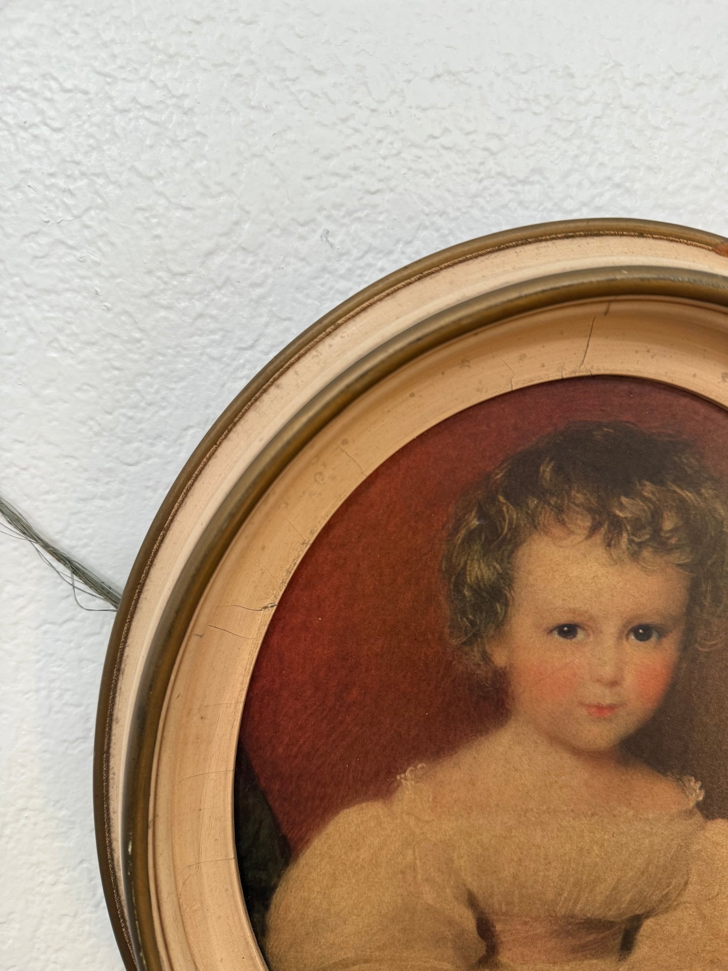 Vintage portrait of a child in a round wooden frame on a textured white wall.