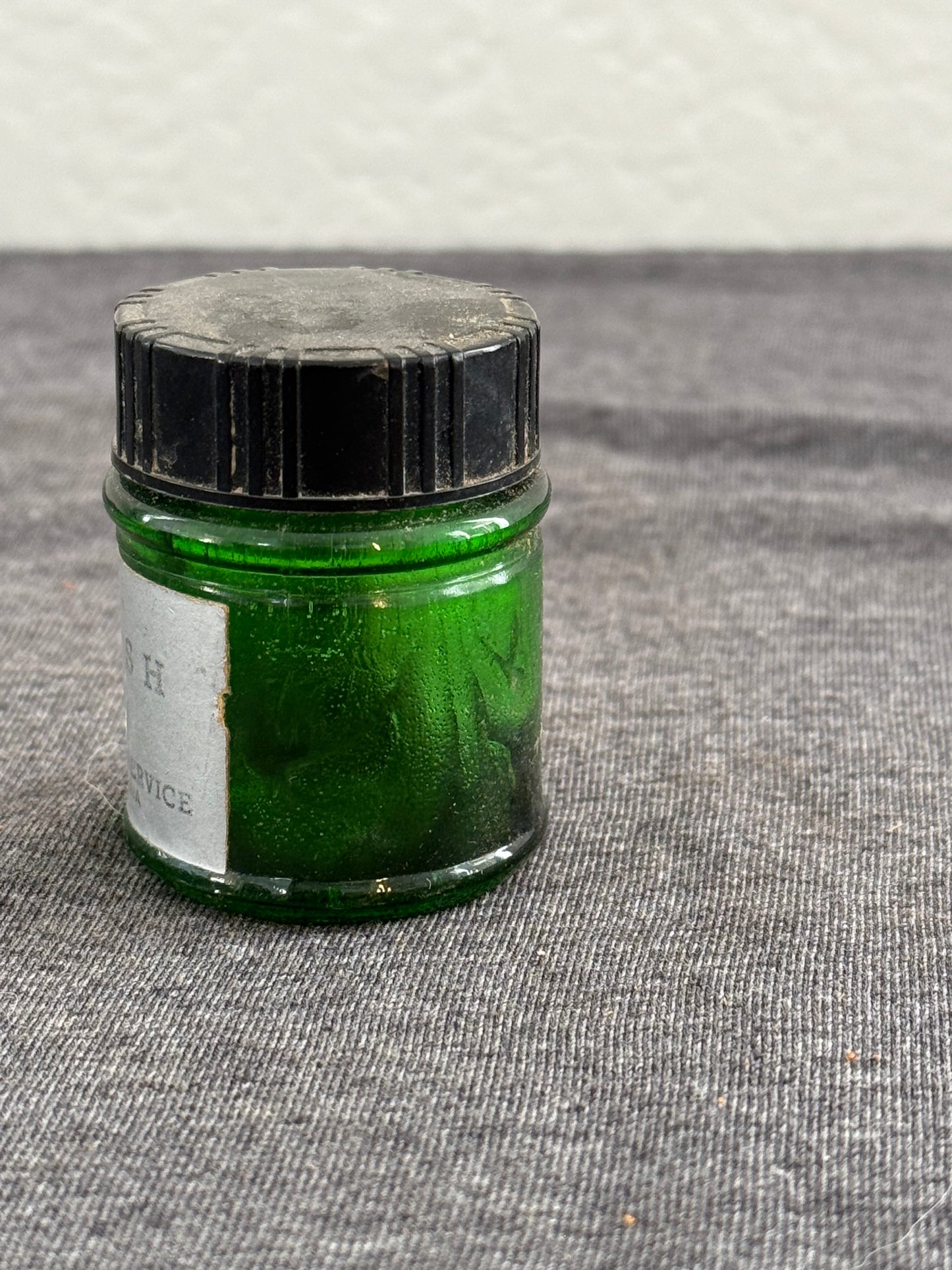 Small green container with a black lid on a textured surface