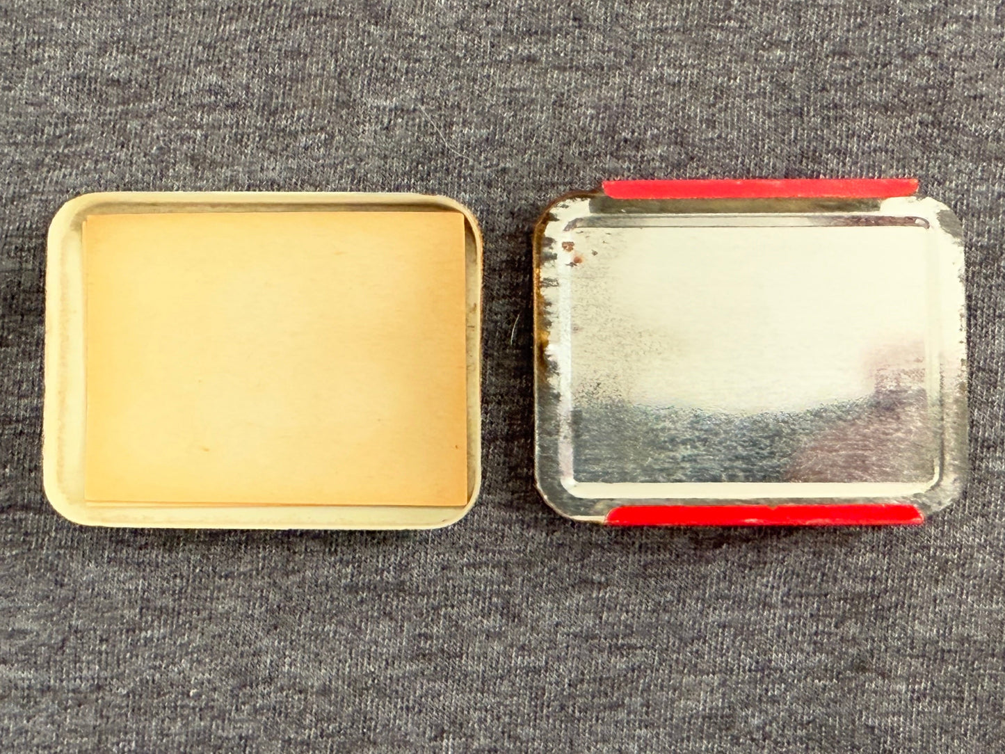 Two metal containers, one gold and one silver with red accents, on a gray textured surface.