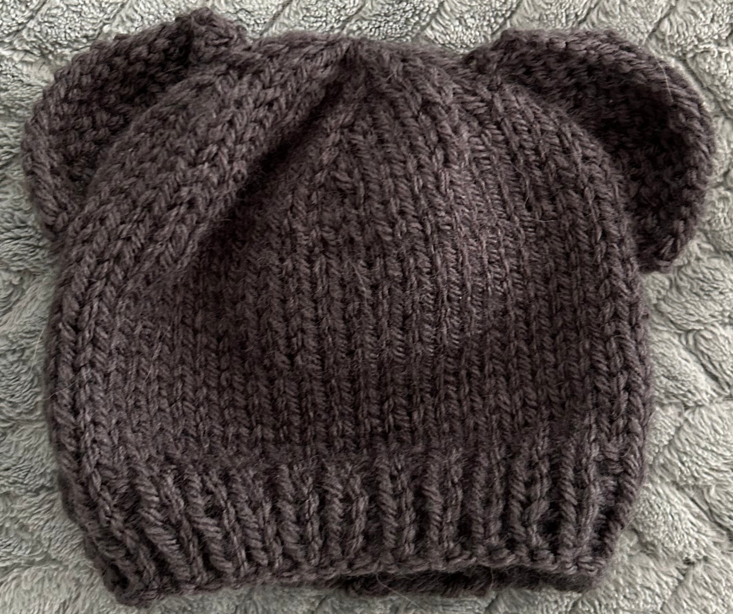 Knitted brown hat with bear ears on a textured gray surface