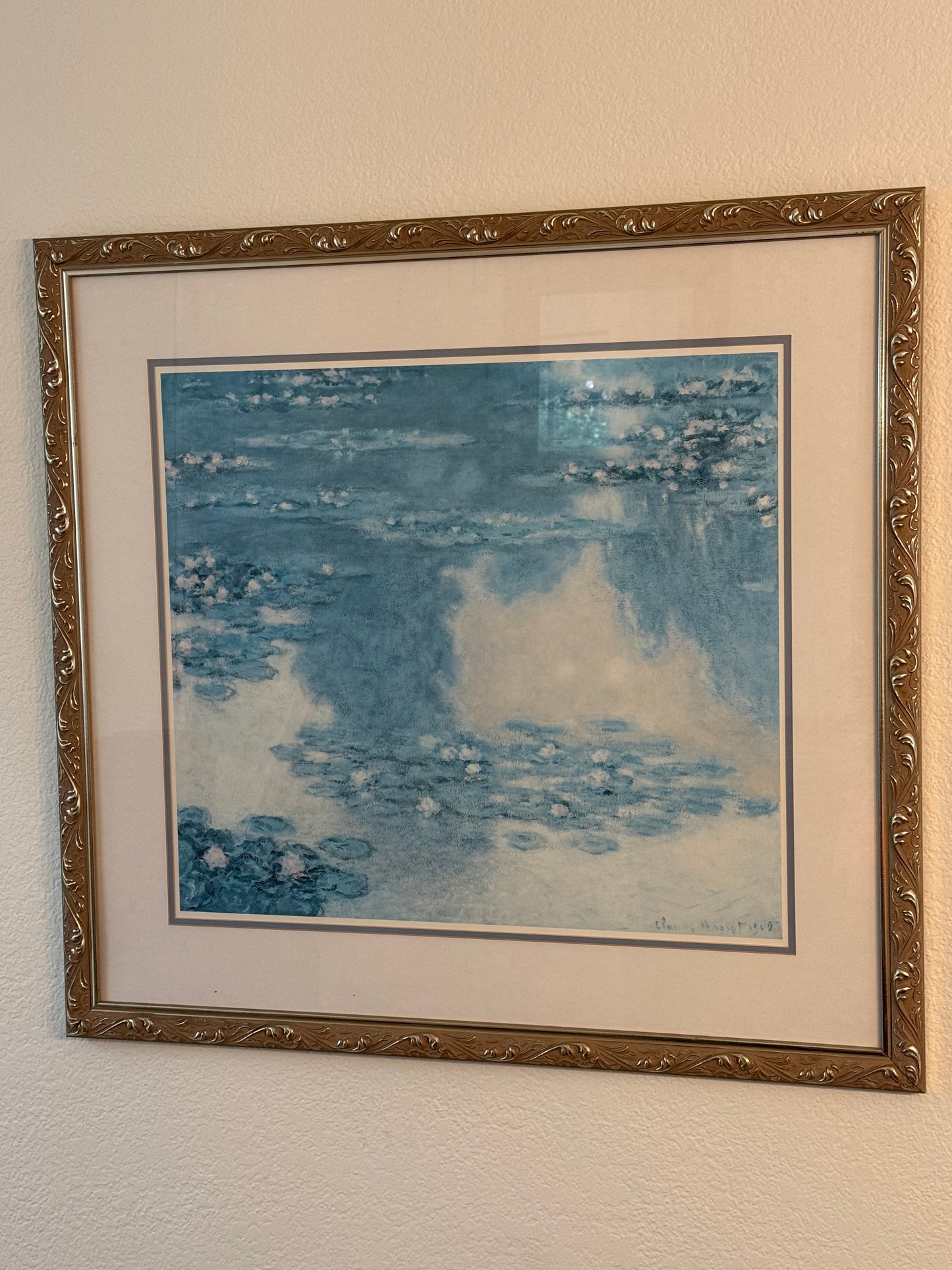 Framed reproduction of Monet's Water Lillies artwork with abstract blue design on a beige wall