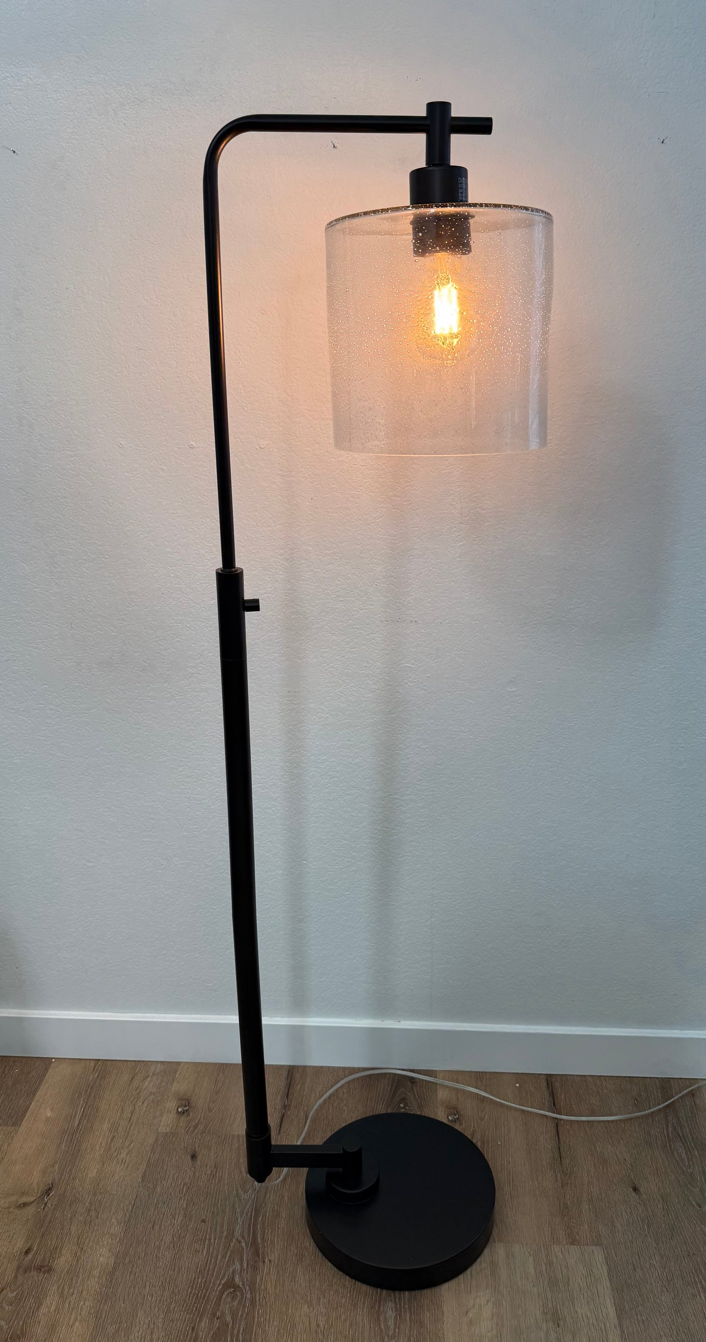 Modern floor lamp with black metal stand and clear glass shade on a light wooden floor.
