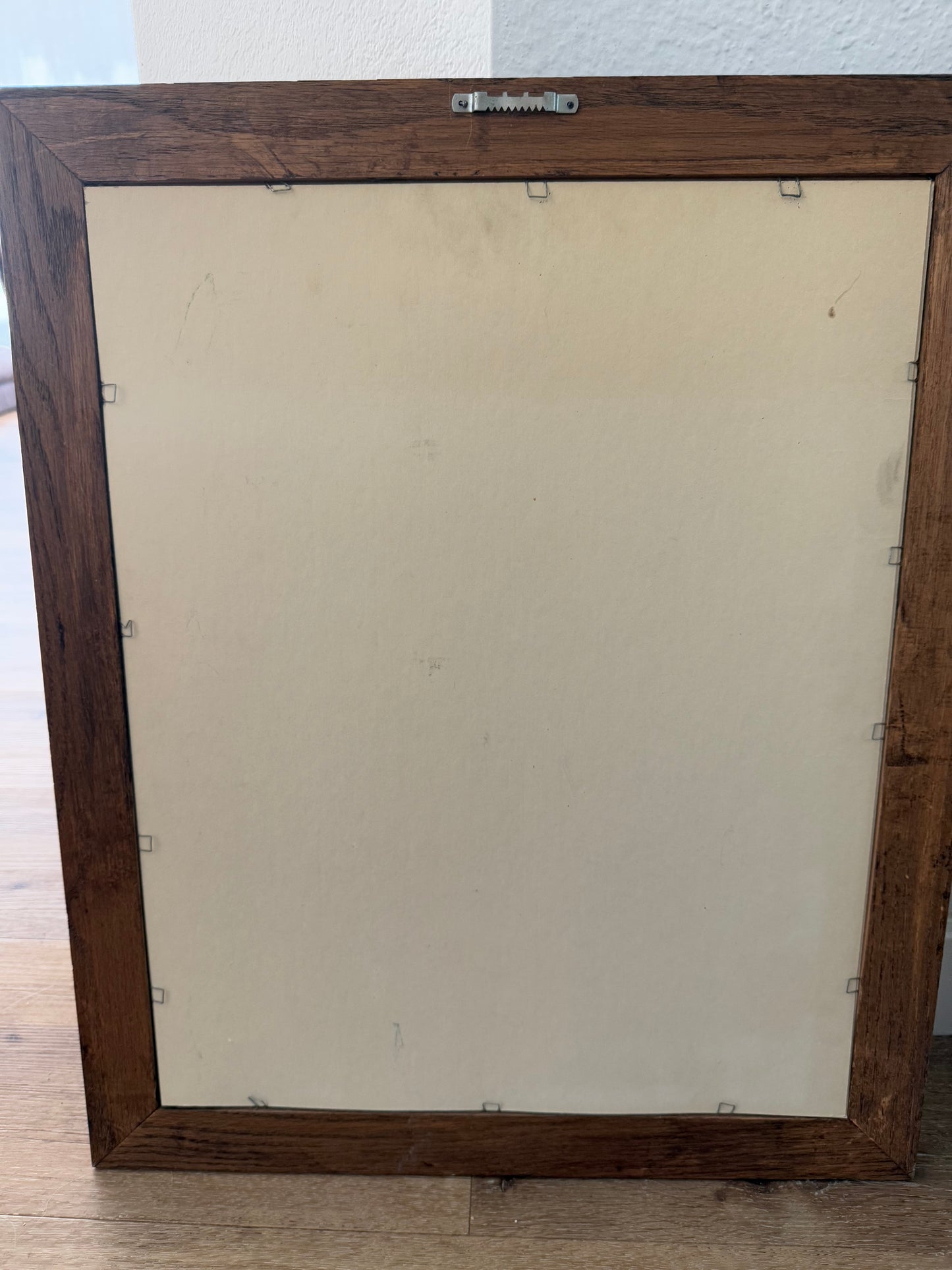 bakside of a Wooden picture frame with a beige interior on a light wooden floor.