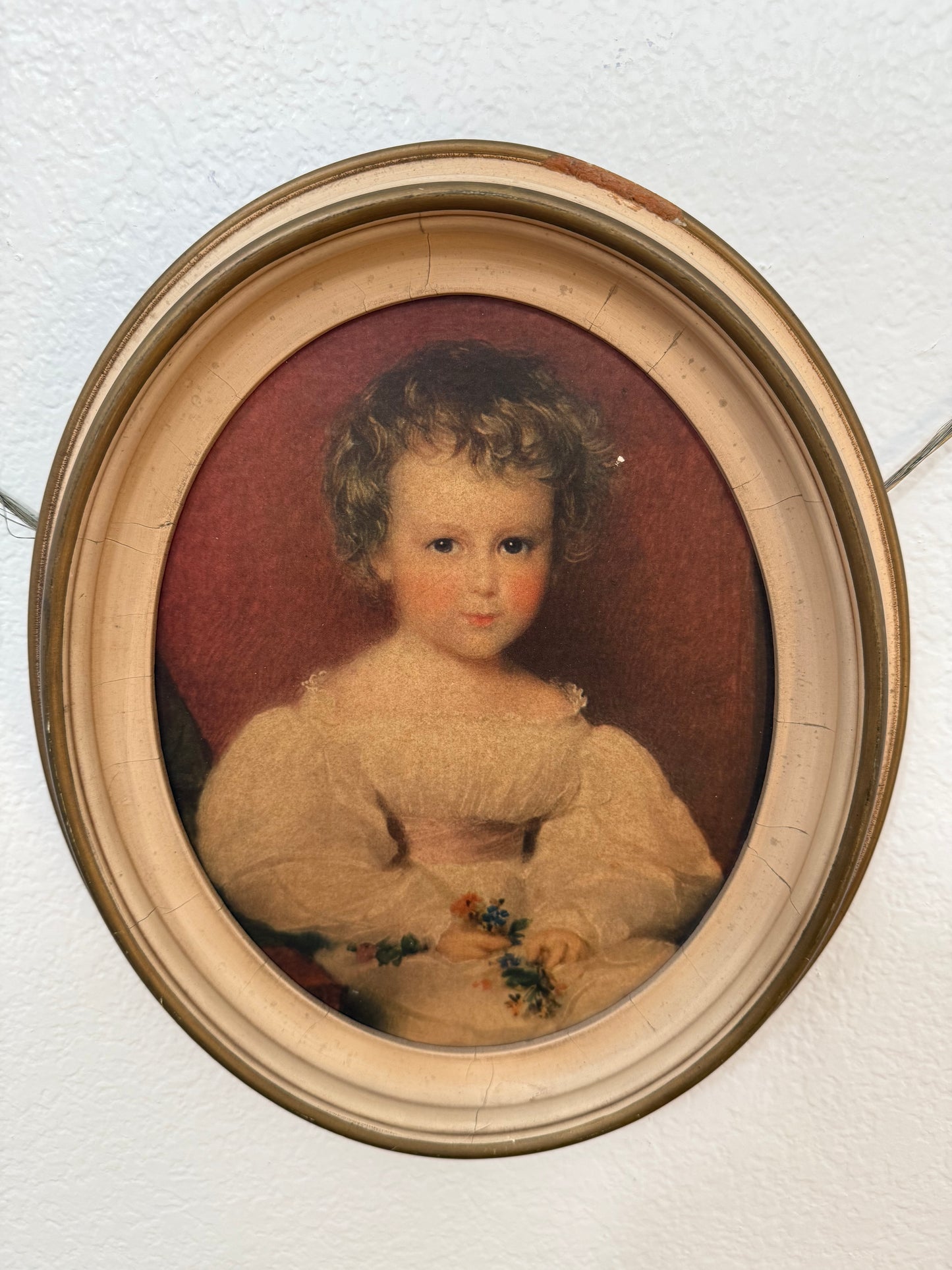 Round portrait of a child in a gold frame on a textured white wall.