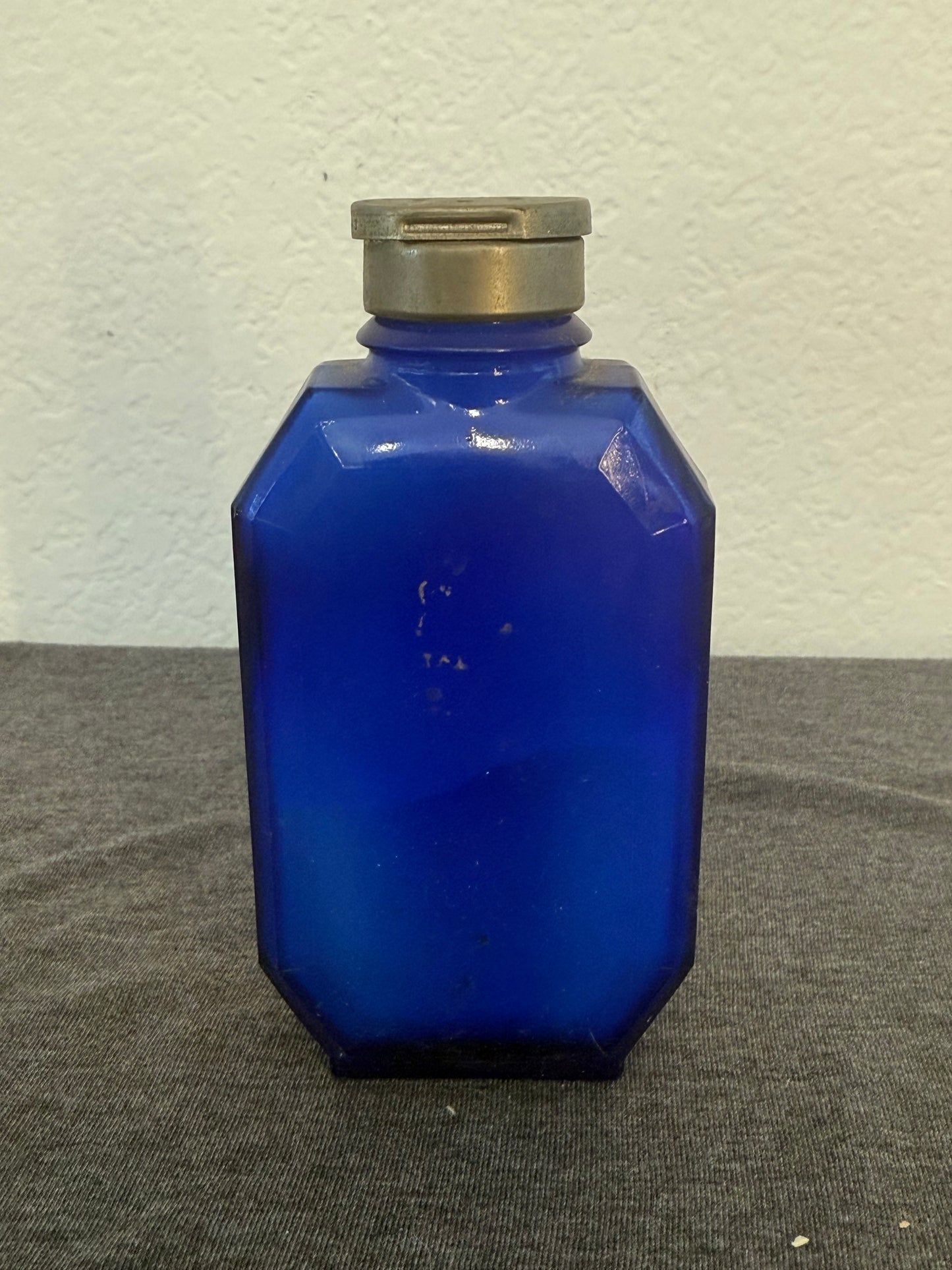 Cobalt blue glass bottle with a metallic cap on a gray and white background