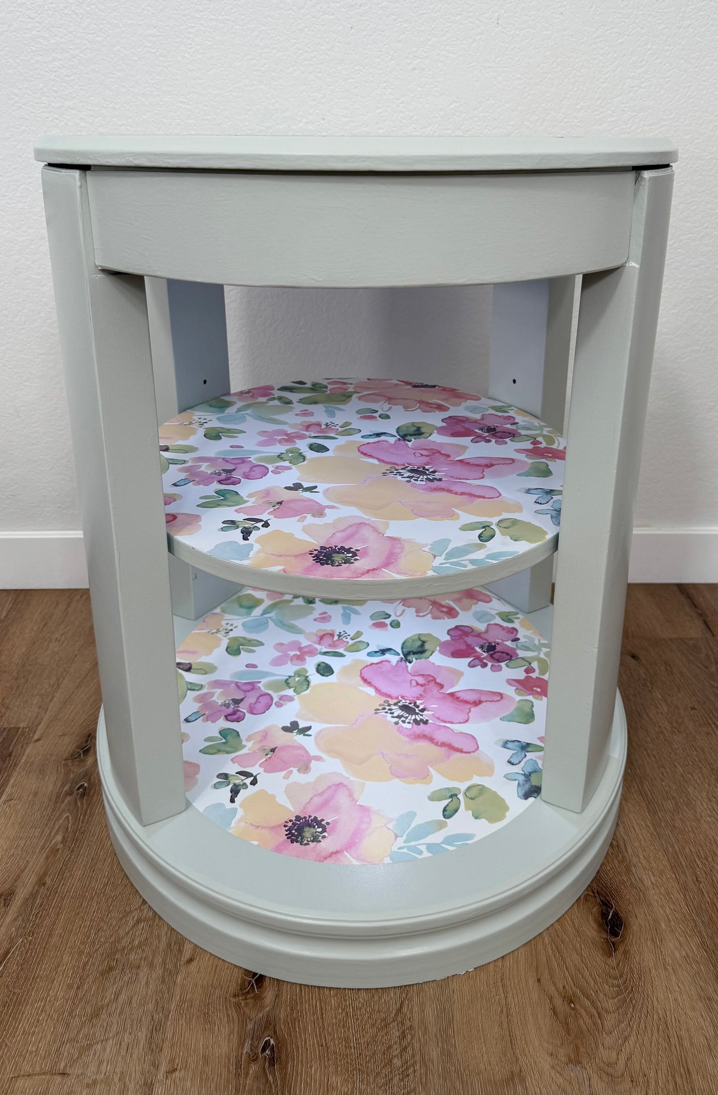 Round gray table with floral-patterned shelves on a wooden floor.