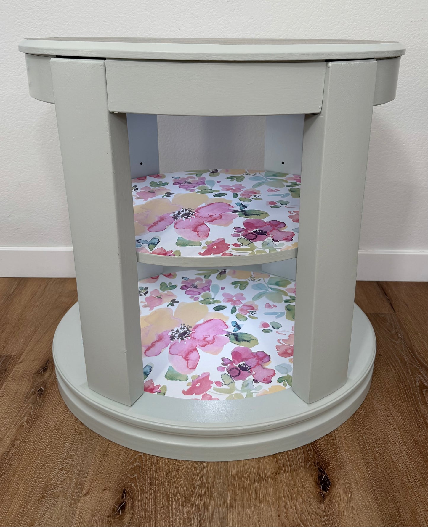 Oval side table with floral-patterned shelves on a wooden floor.