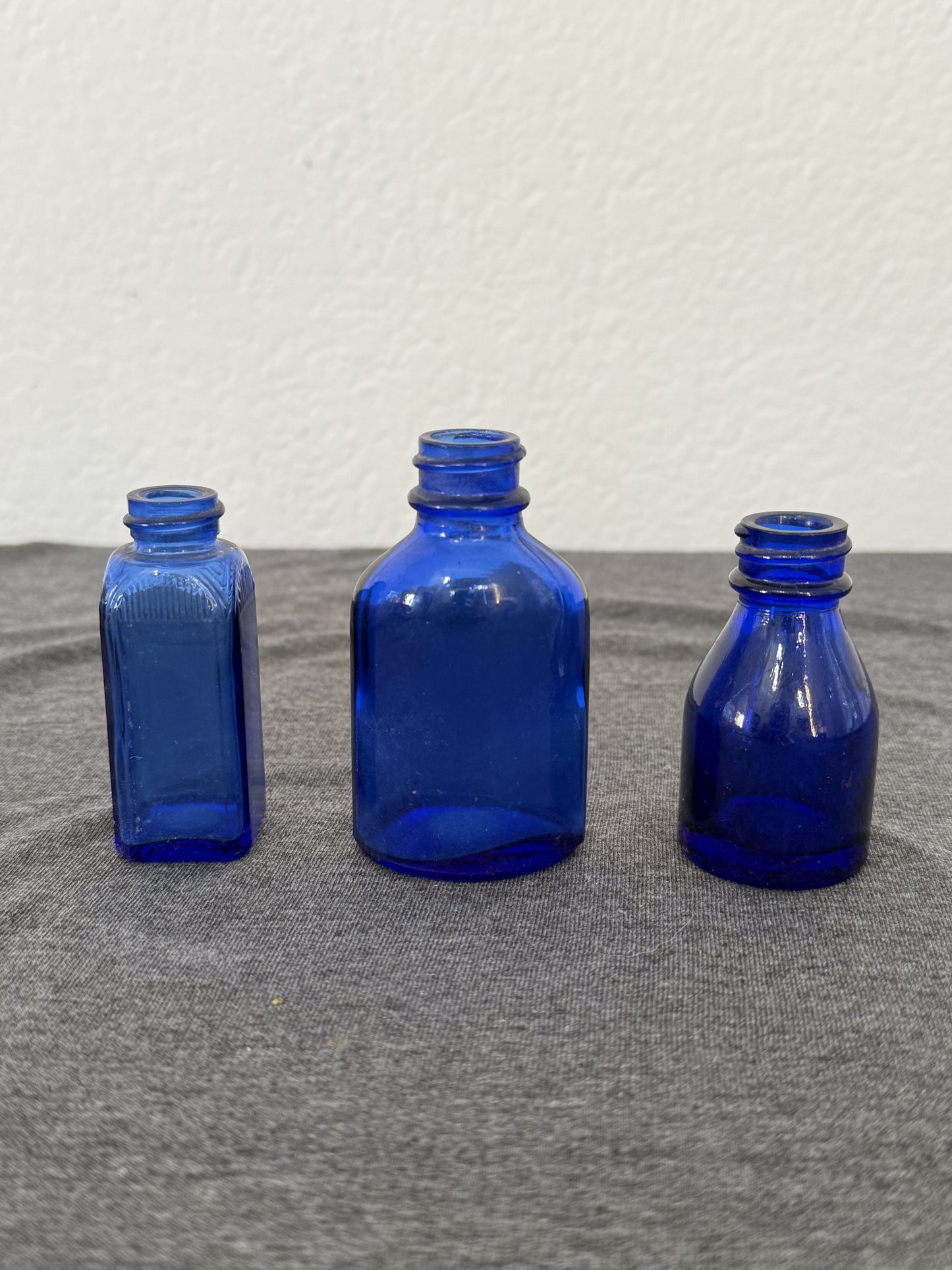Three blue glass bottles of different shapes on a gray surface with a white background
