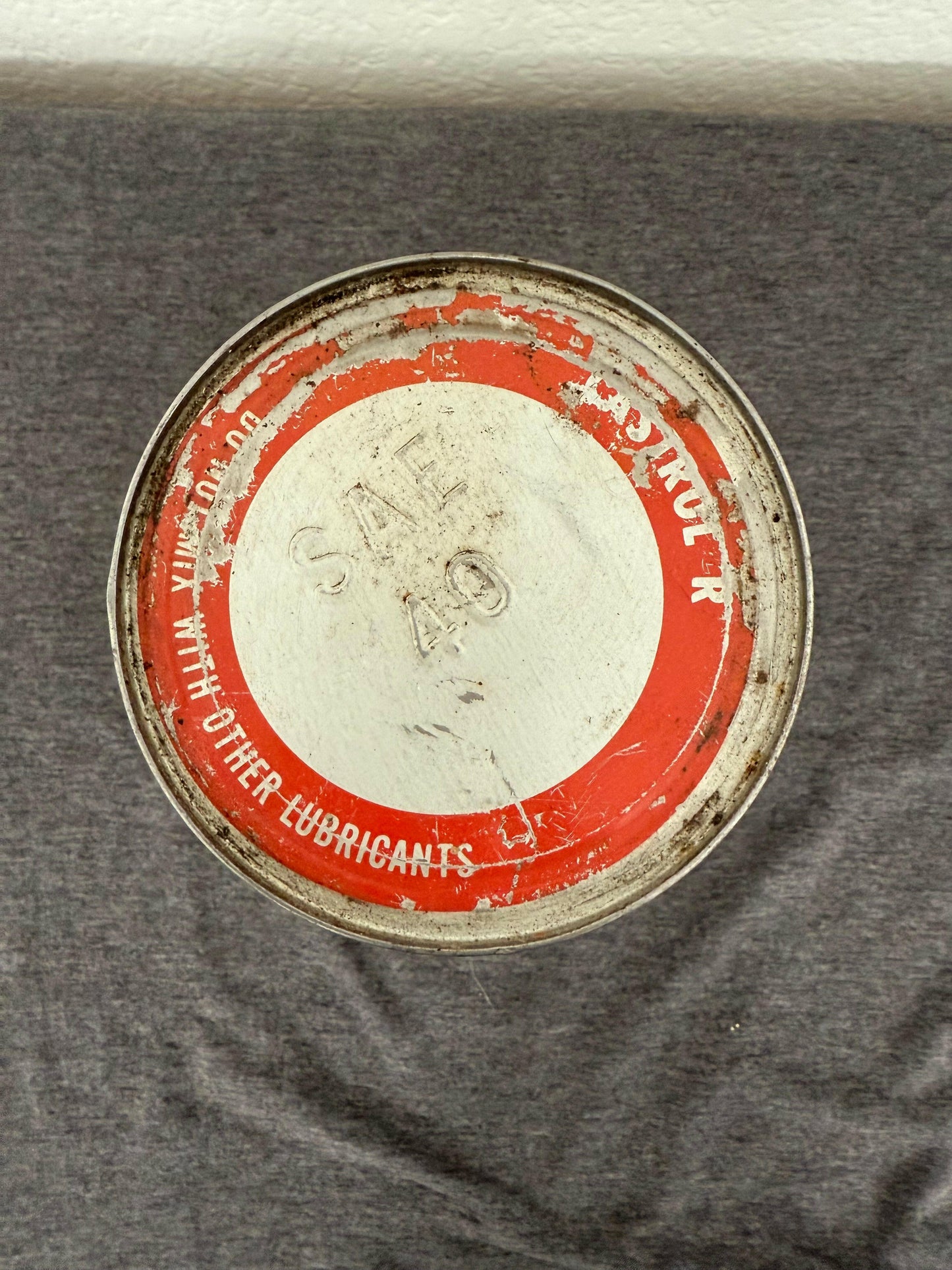 Round metal container with red label on a gray fabric background