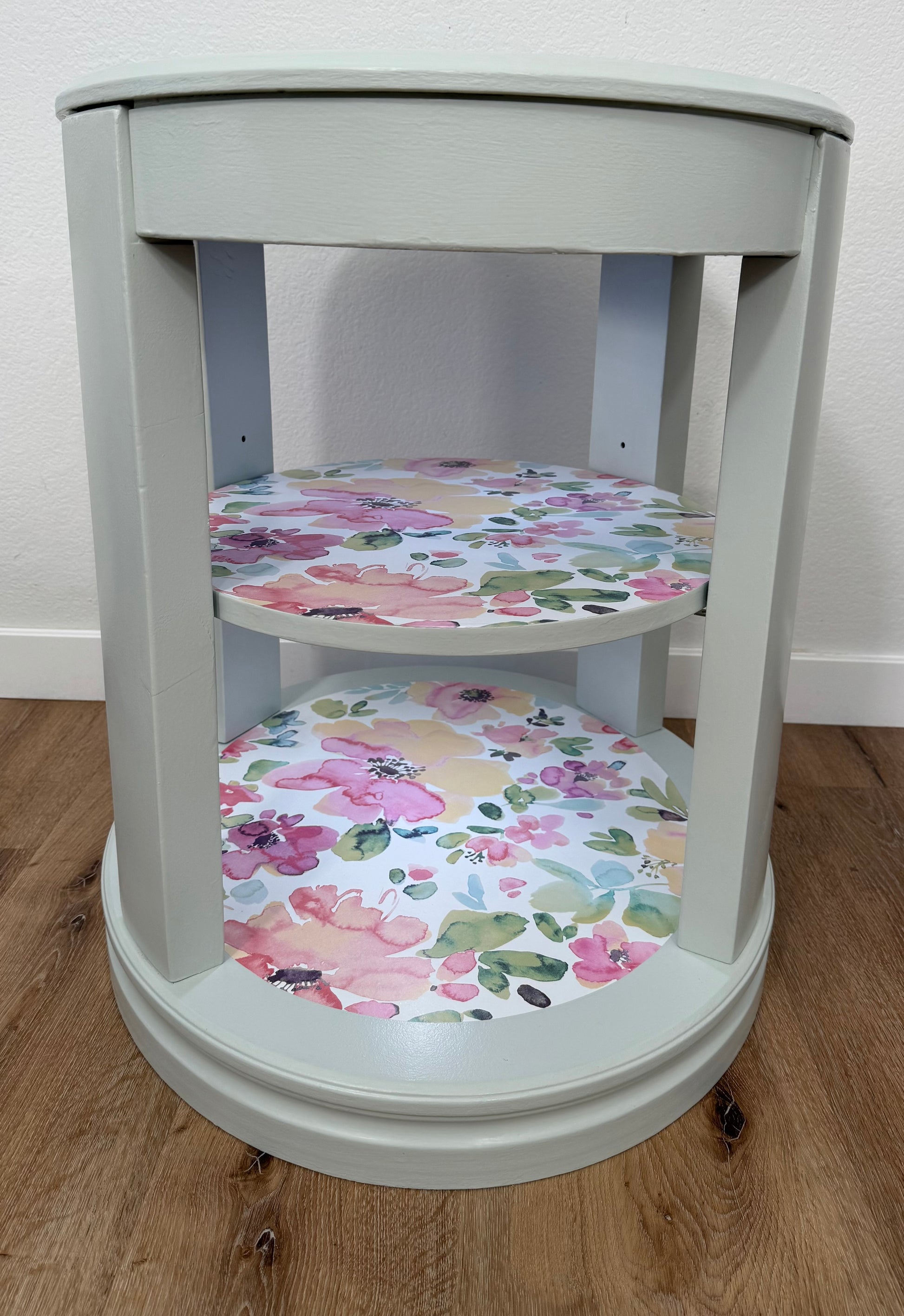 Oval side table with floral-patterned shelves on a wooden floor.