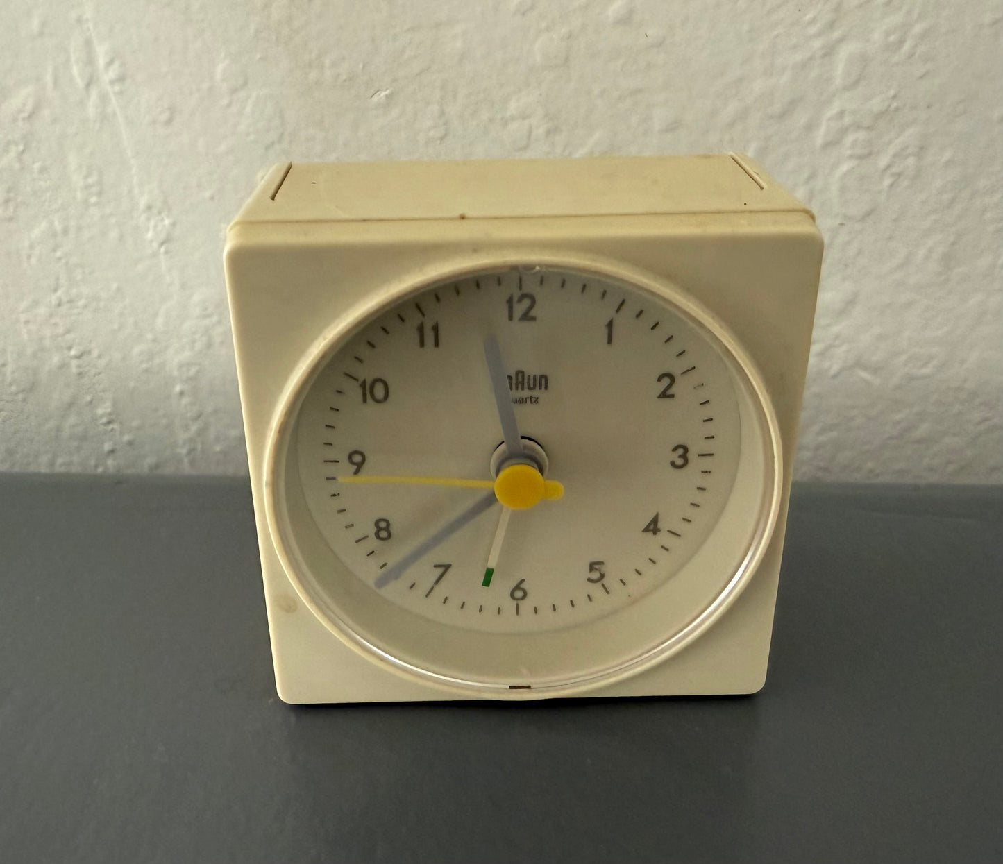 Beige analog alarm clock on a dark surface with a white wall background