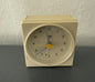 Beige analog alarm clock on a dark surface with a white wall background