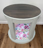 Oval wooden side table with floral patterned shelves on a wooden floor.